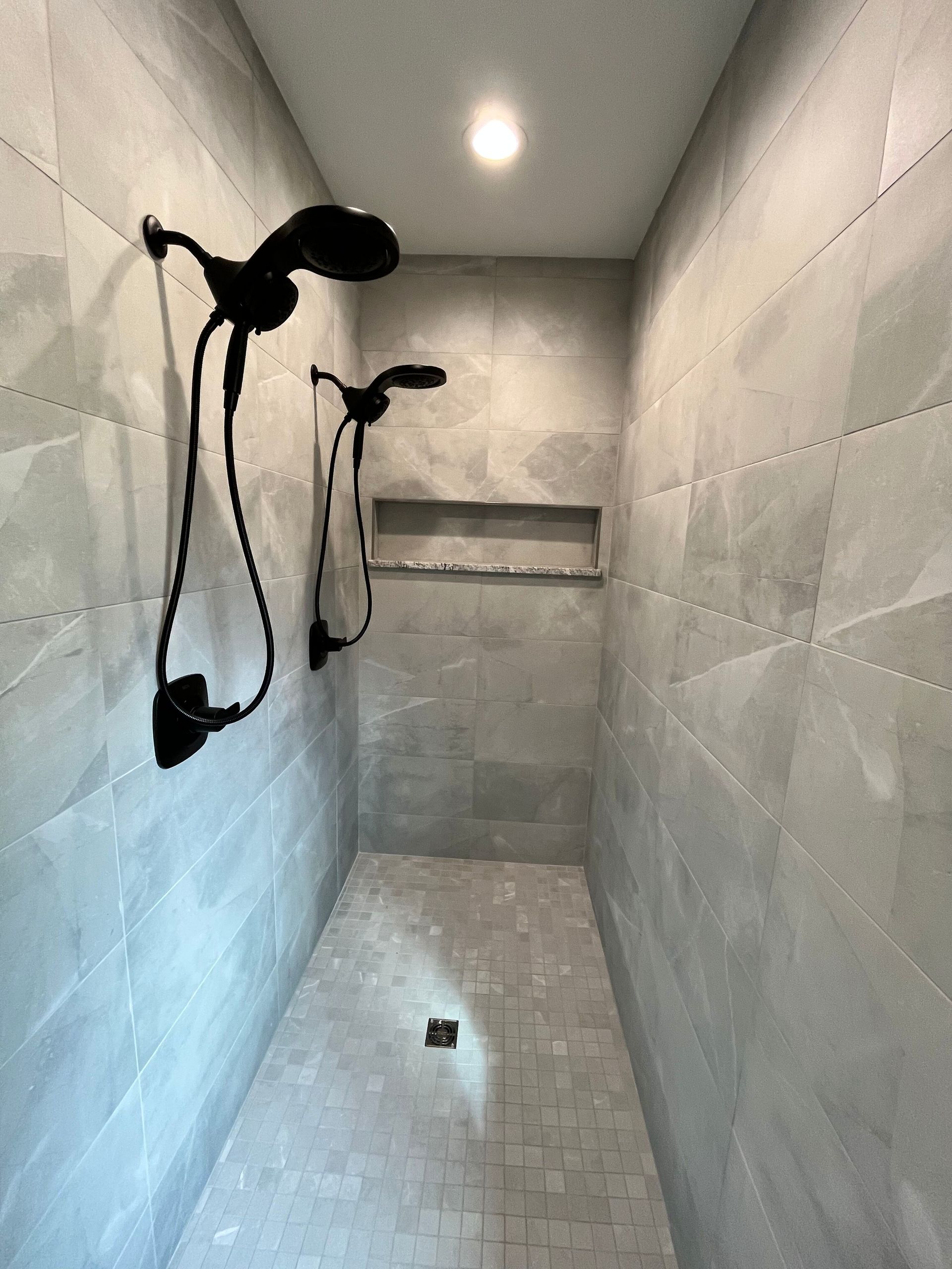 A shower with two shower heads and a shelf on the wall.
