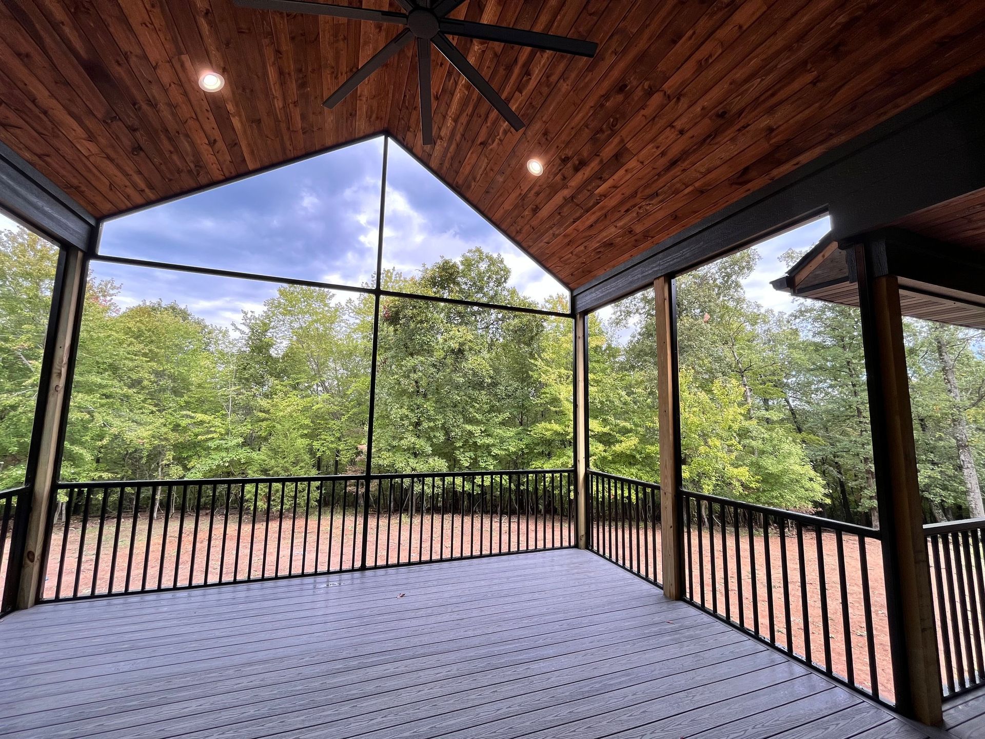 A screened in porch with a ceiling fan and a view of trees.
