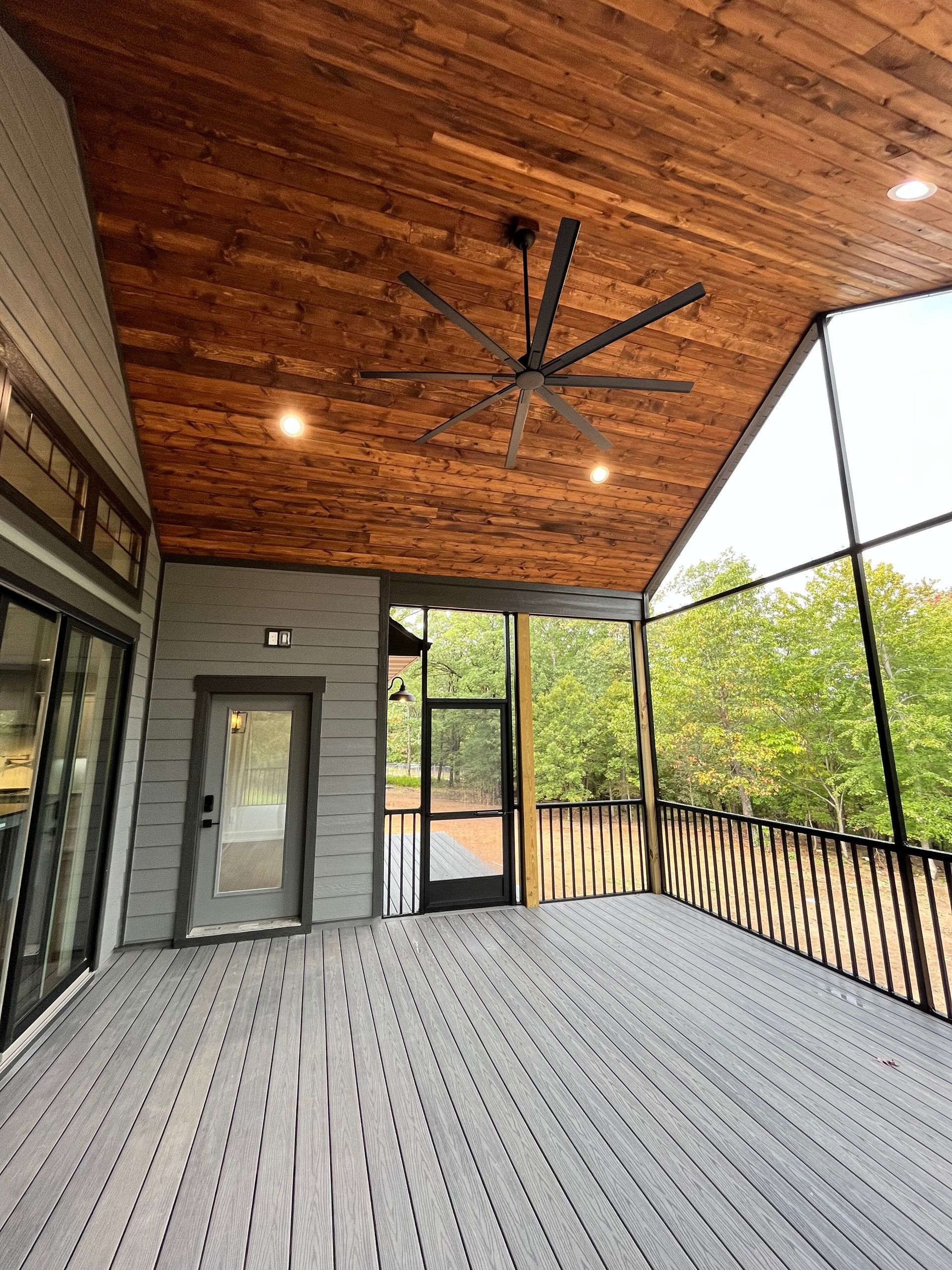 A screened in porch with a wooden ceiling and a ceiling fan.