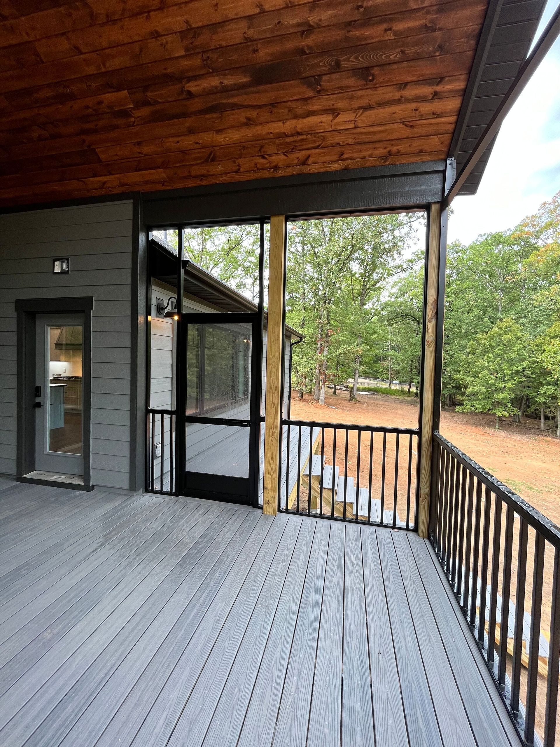 A screened in porch with a wooden ceiling and a black door.
