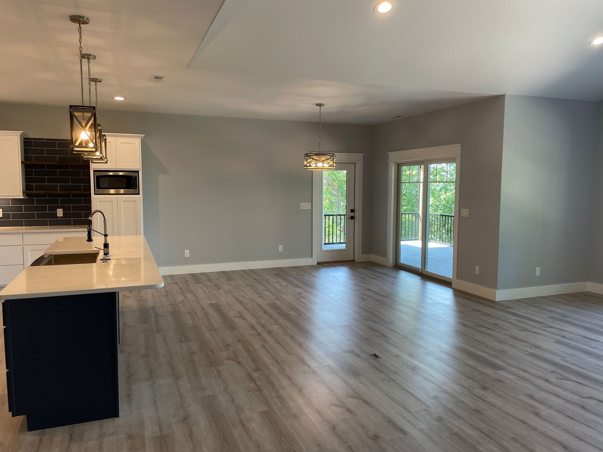A large empty room with a kitchen and sliding glass doors.