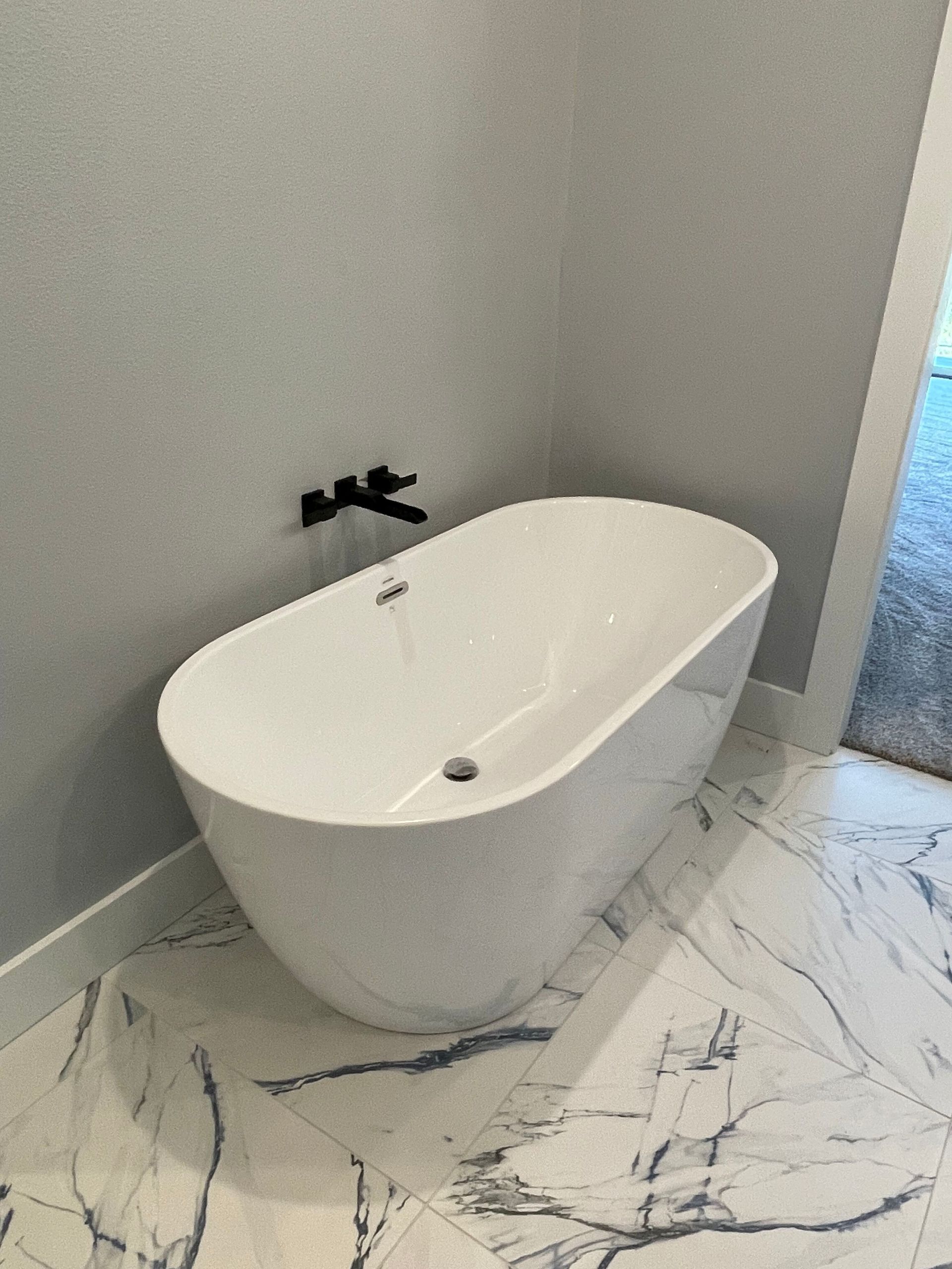 A white bathtub is sitting on a marble floor in a bathroom.