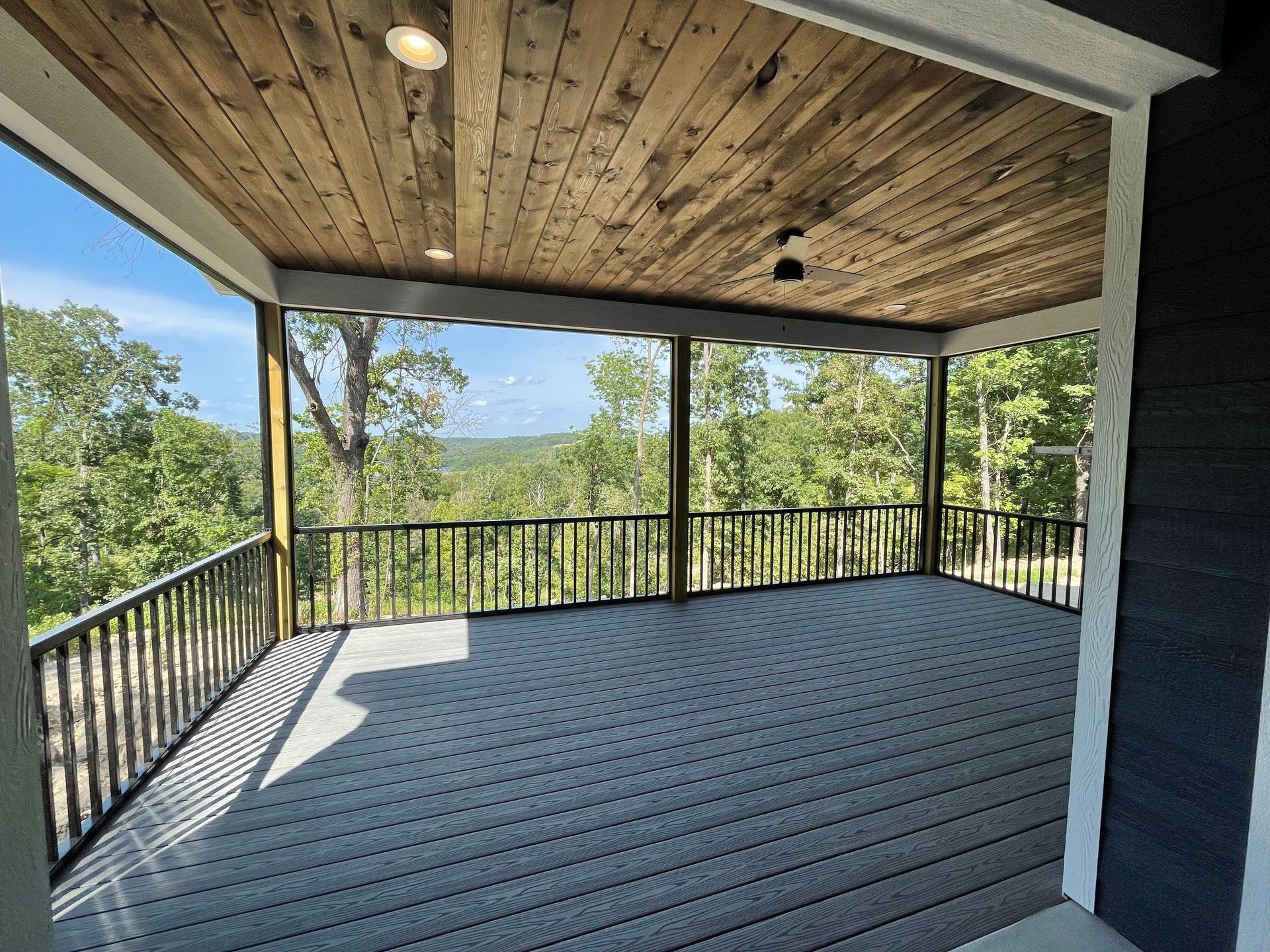 A screened in porch with a wooden ceiling and a view of trees.