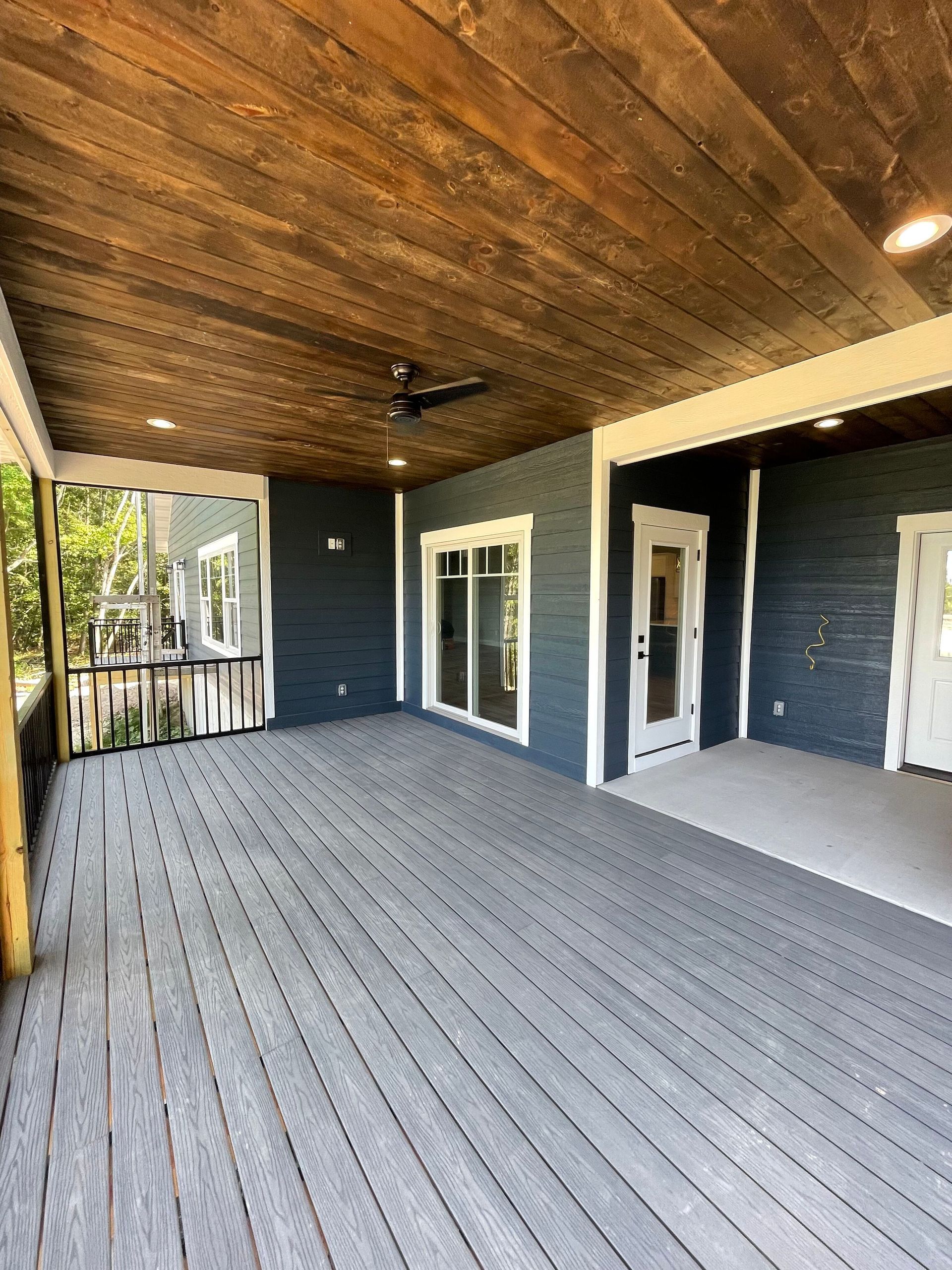 A large screened in porch with a wooden ceiling and a ceiling fan.
