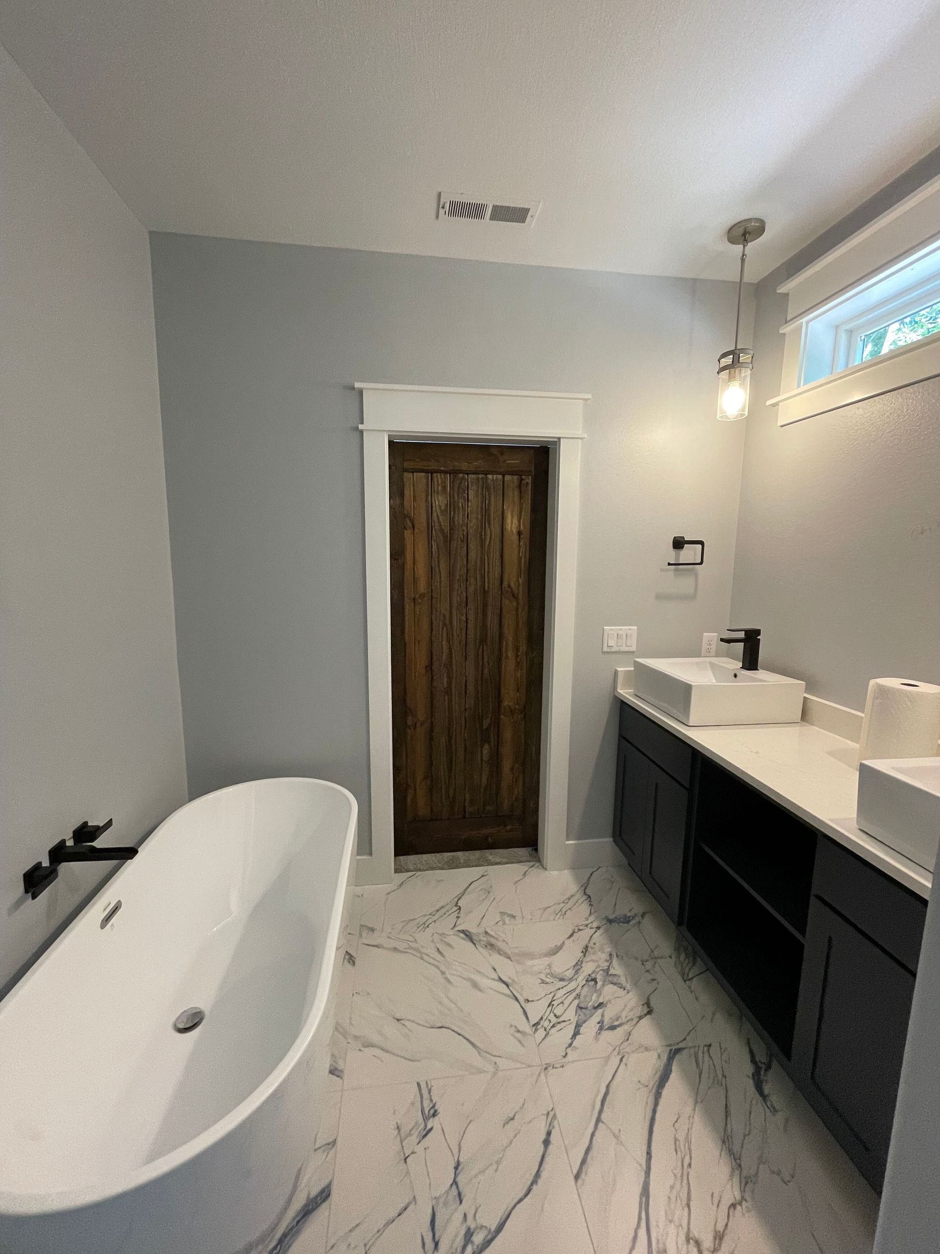 A bathroom with two sinks , a tub , and a wooden door.