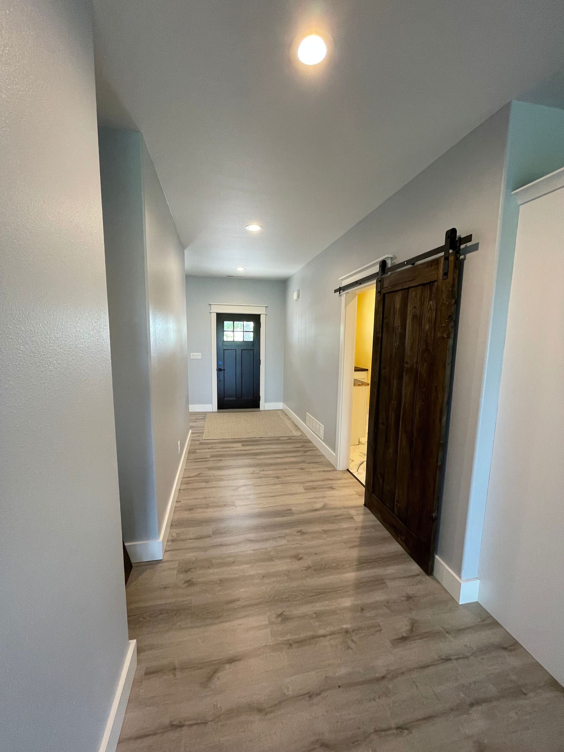 A hallway with a sliding barn door and a black door.
