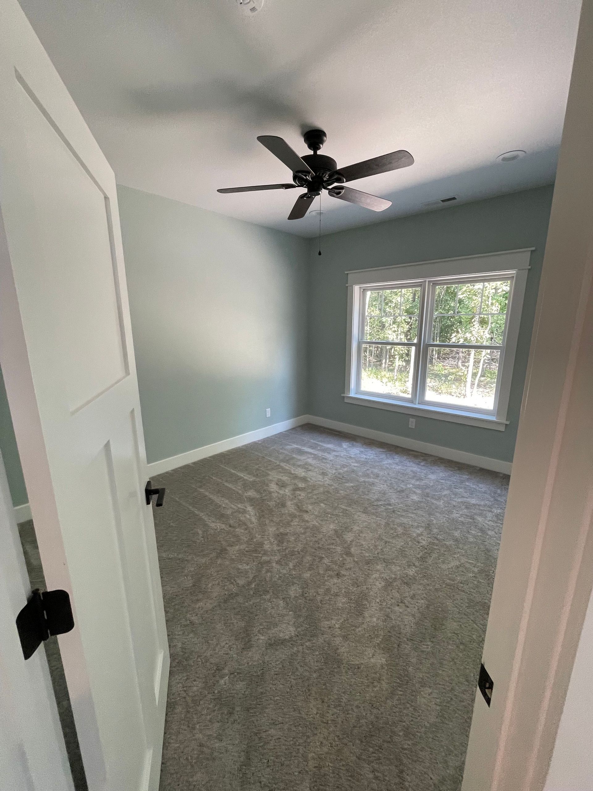 An empty bedroom with a ceiling fan and two windows.