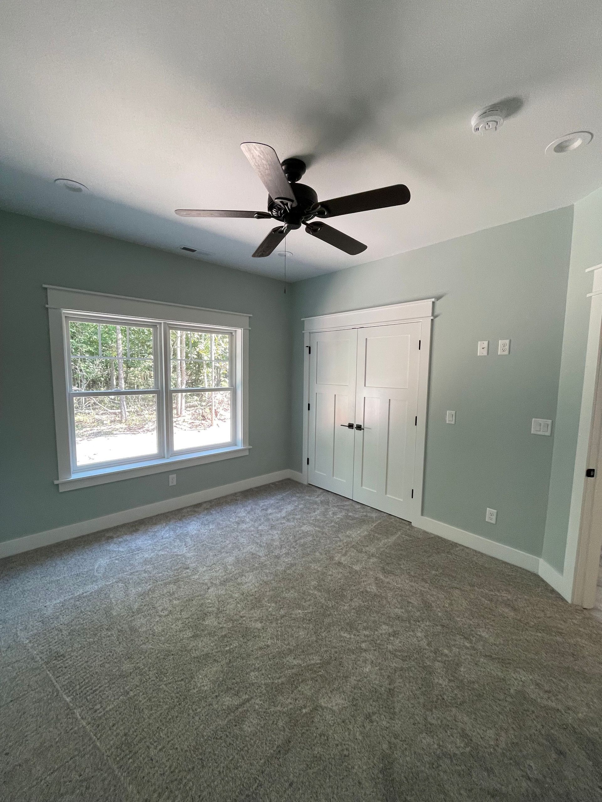 An empty bedroom with a ceiling fan and a window.