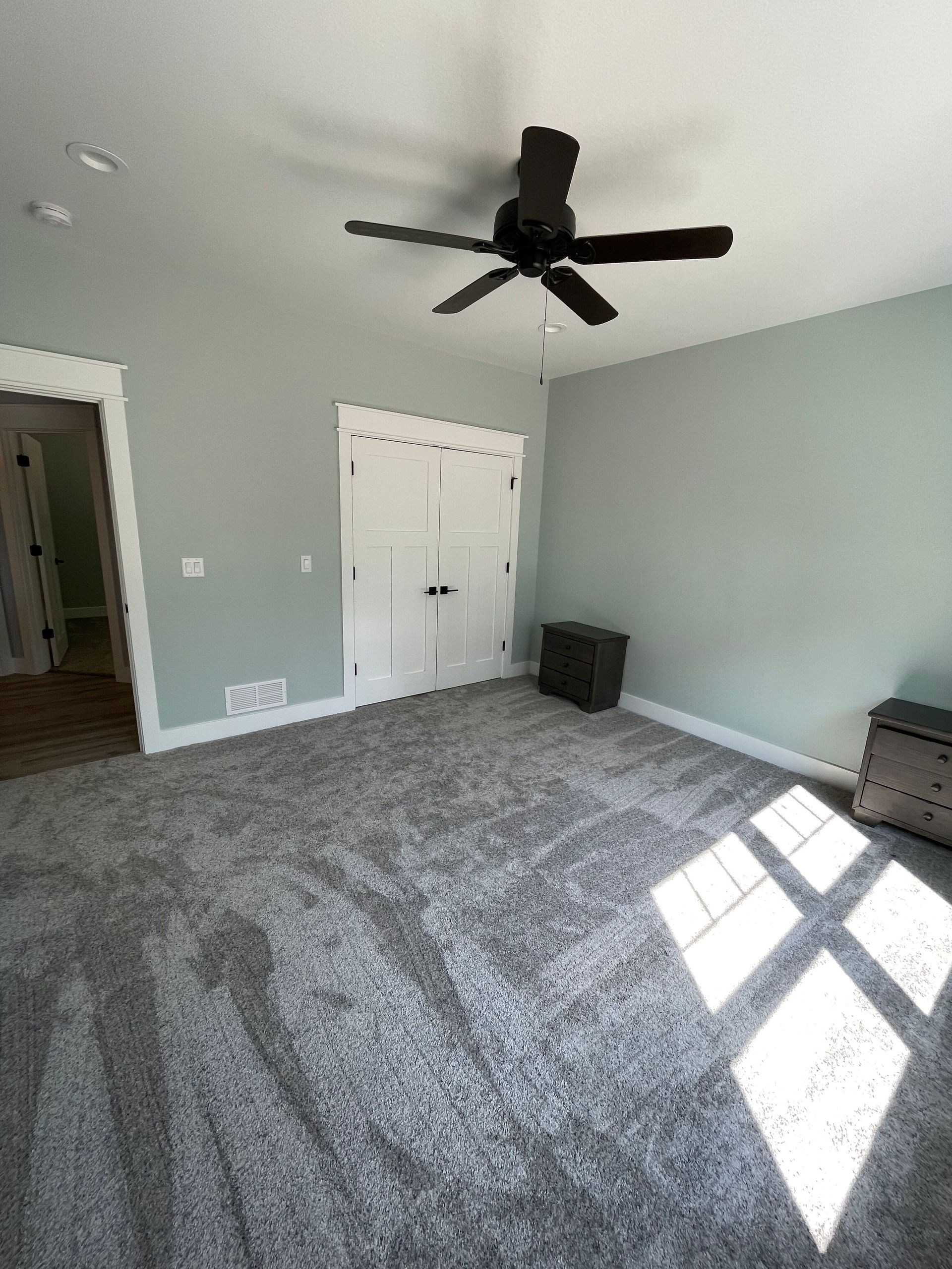 A bedroom with a ceiling fan and a gray carpet.