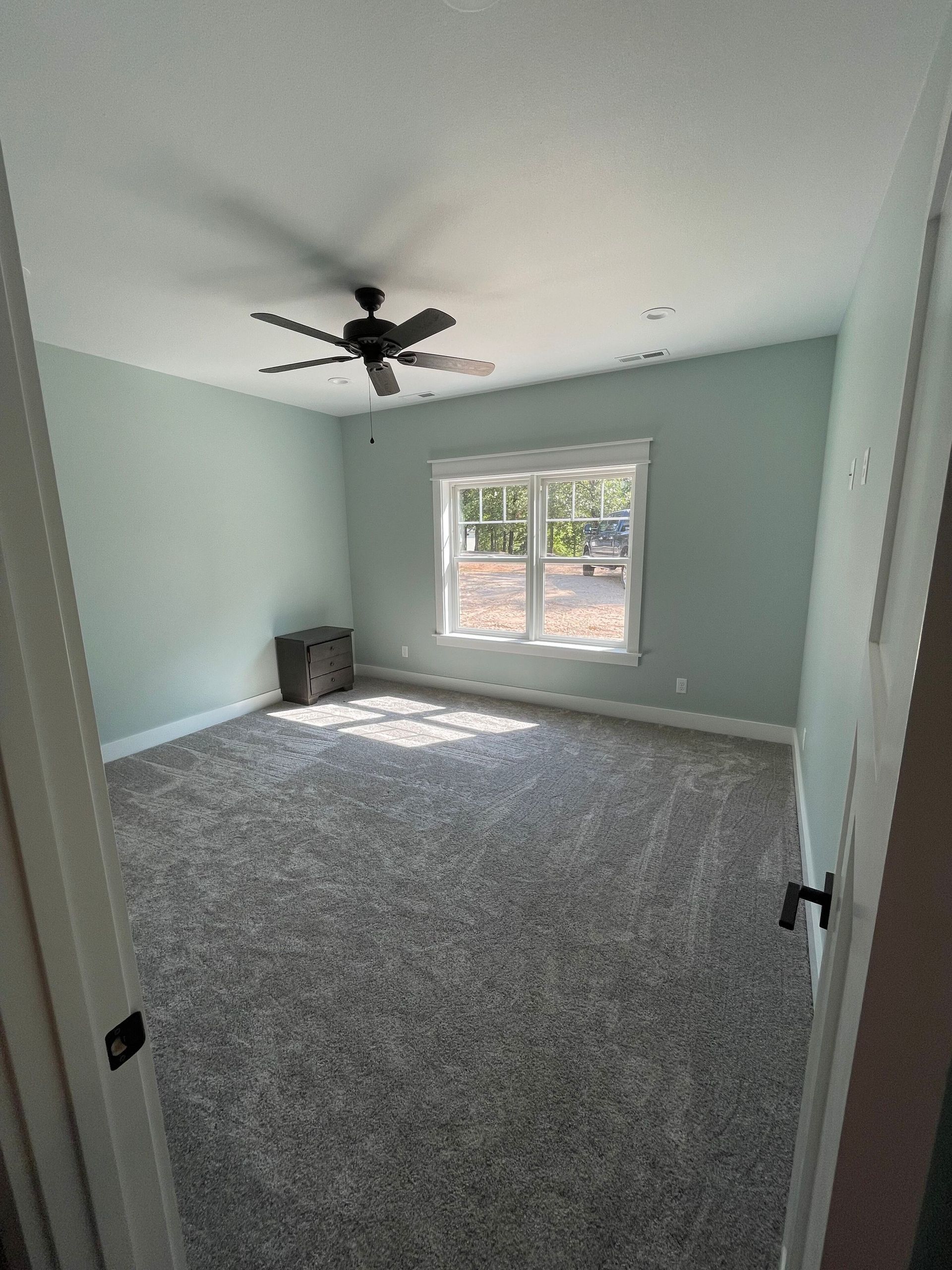 An empty bedroom with a ceiling fan and two windows.