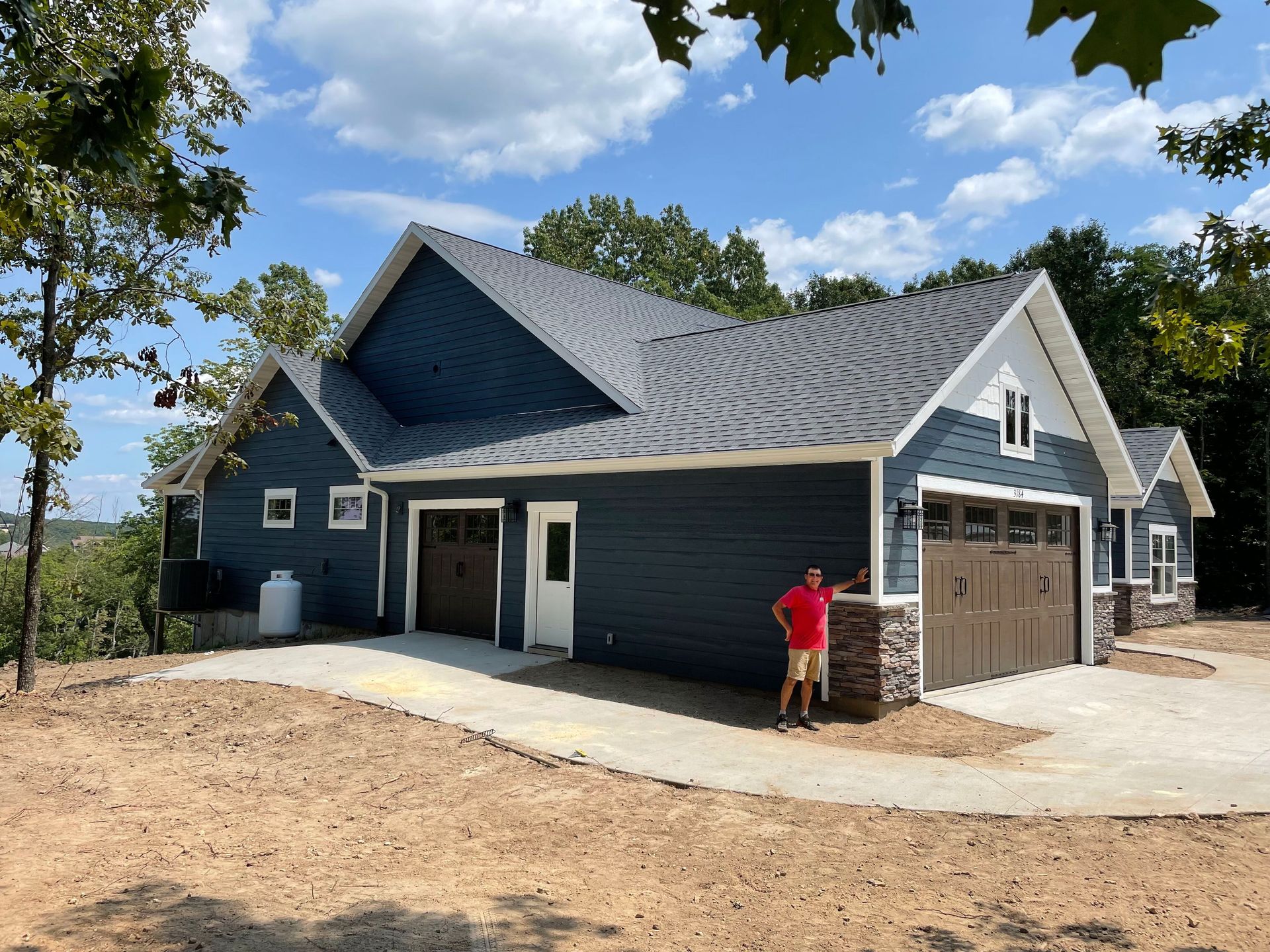A man in a red shirt is standing in front of a blue house.