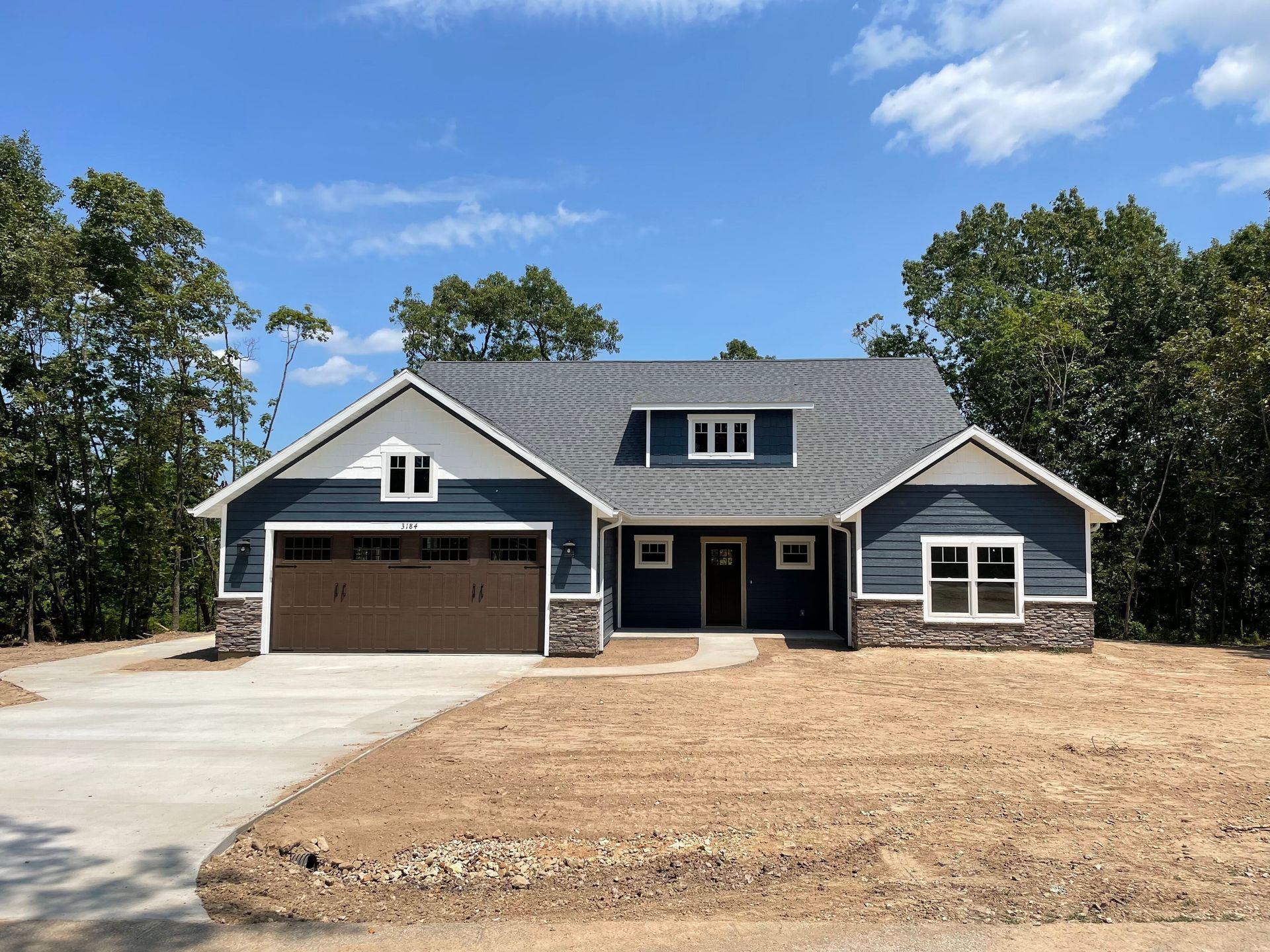 A blue house with a brown garage door is sitting on top of a dirt field.