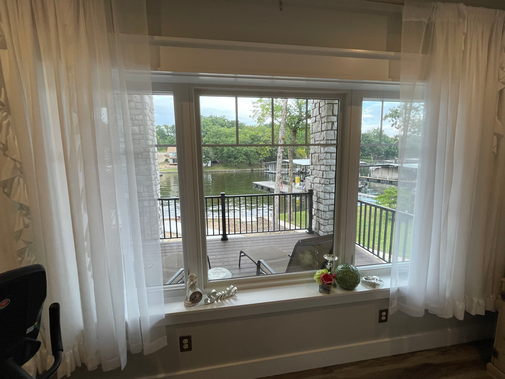 A living room with a large window with white curtains and a view of a lake.