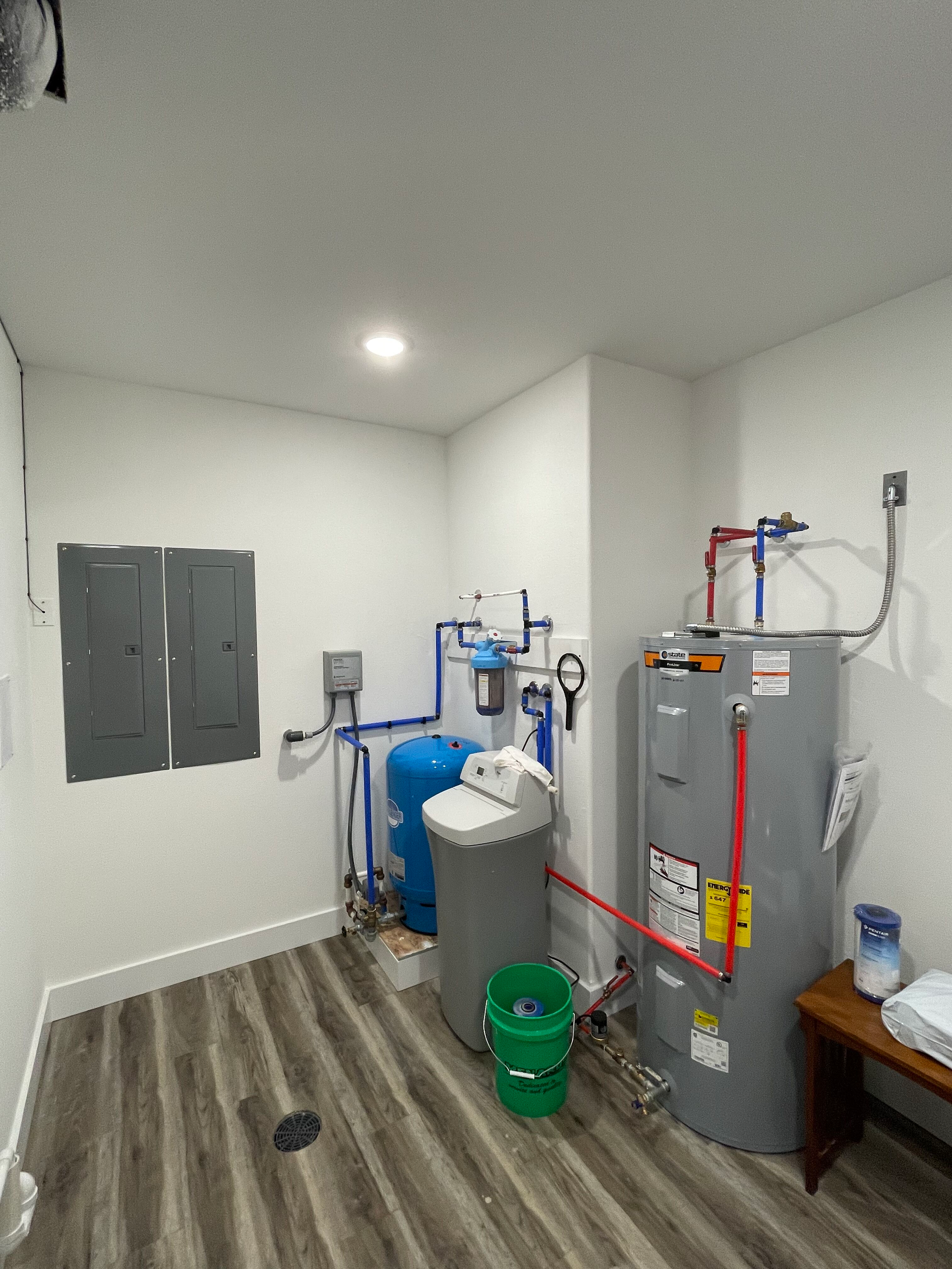 A room with a water heater , buckets , and a bench.