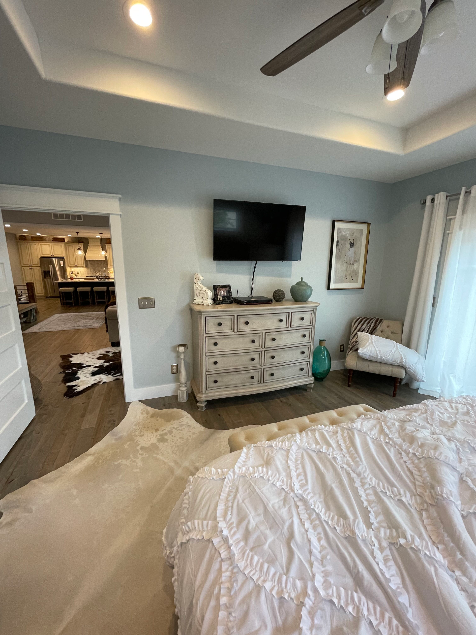 A bedroom with a bed , dresser , television and ceiling fan.