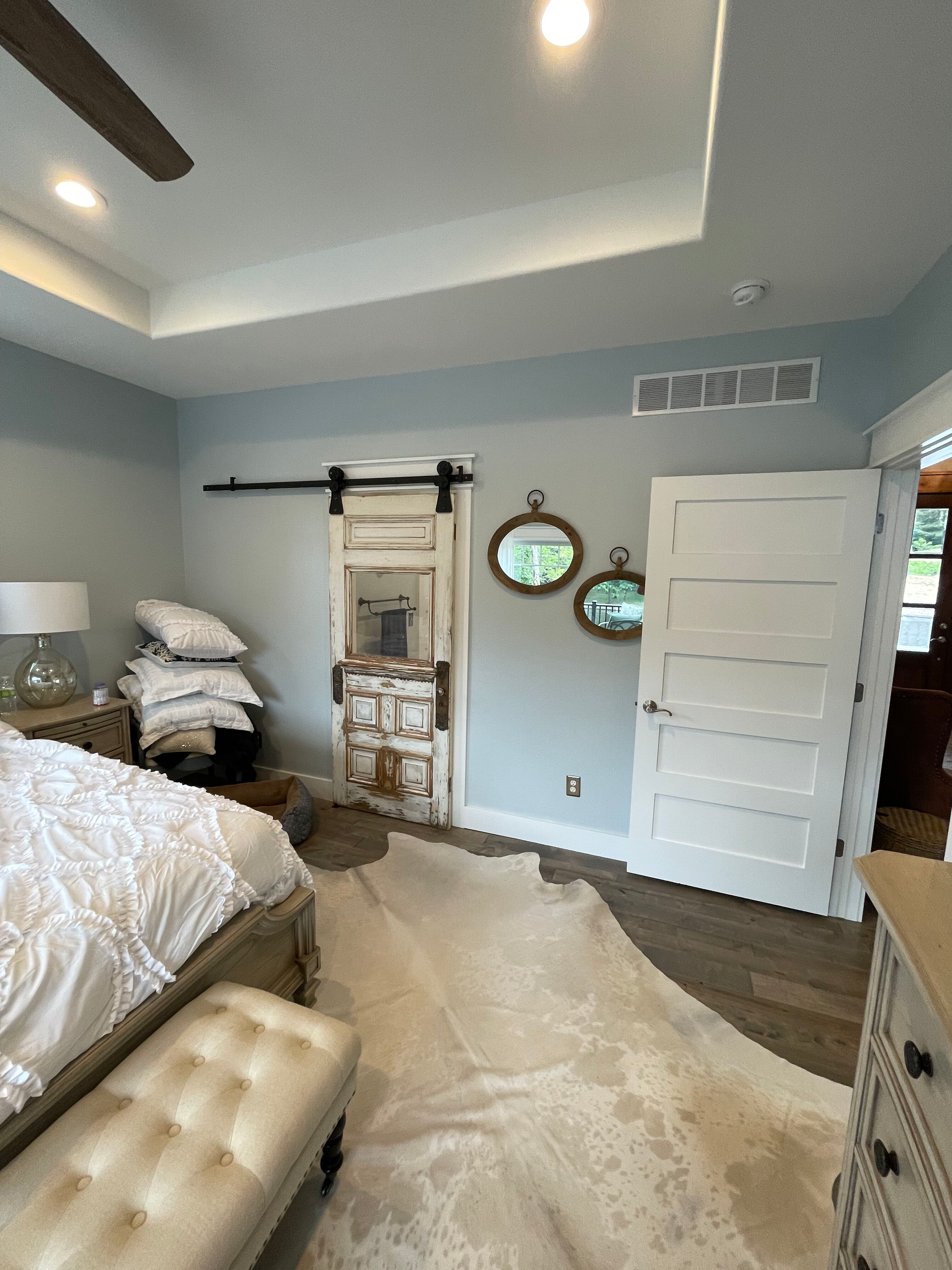 A bedroom with a bed , dresser , bench , mirrors and a ceiling fan.