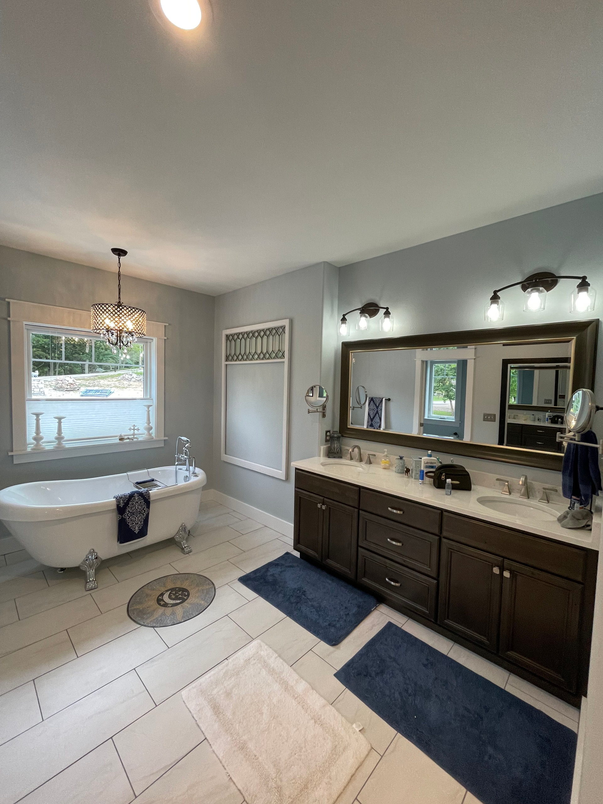 A bathroom with a tub , sink , mirror and window.