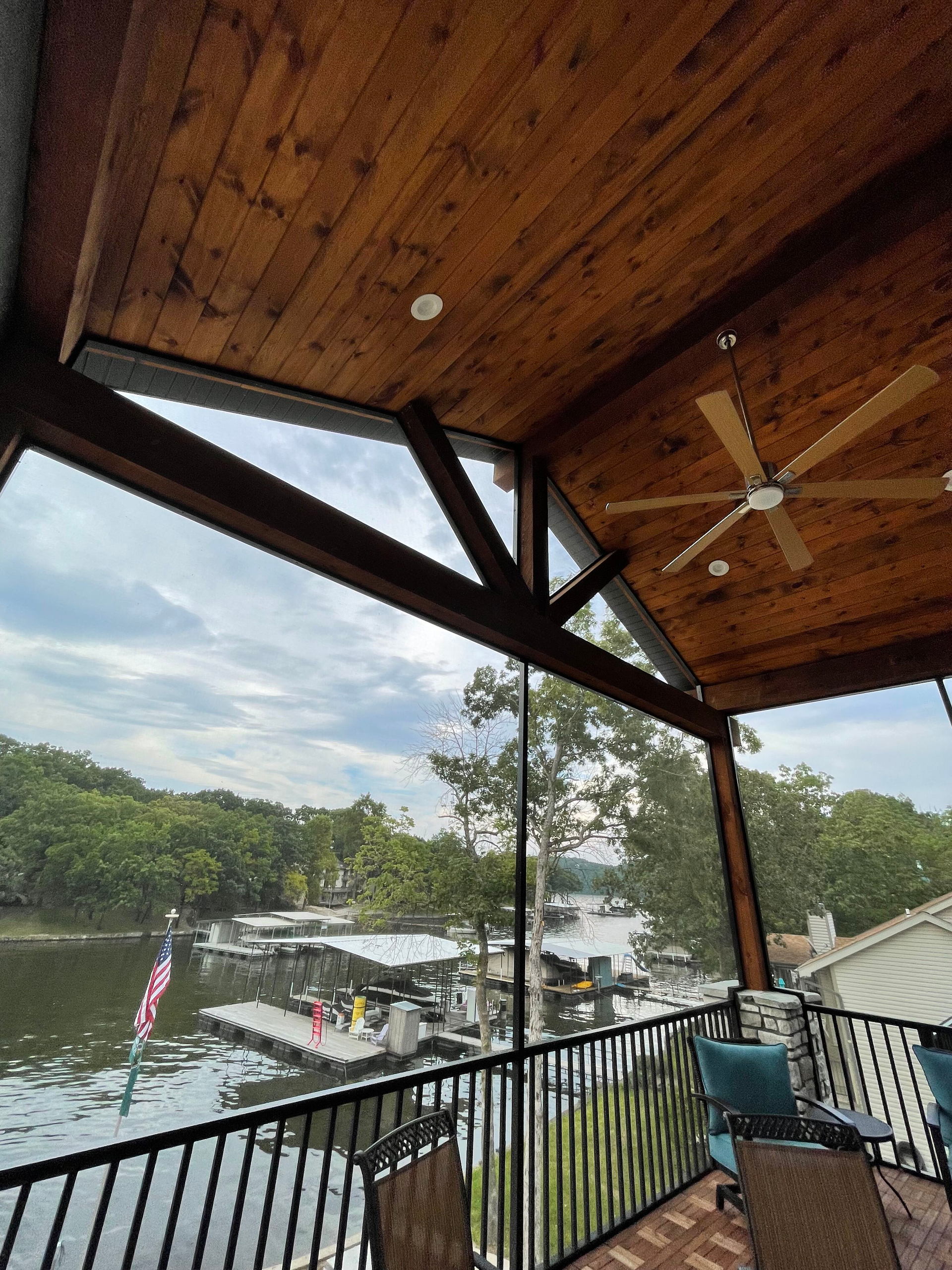 A screened in porch with a view of a lake and a ceiling fan.