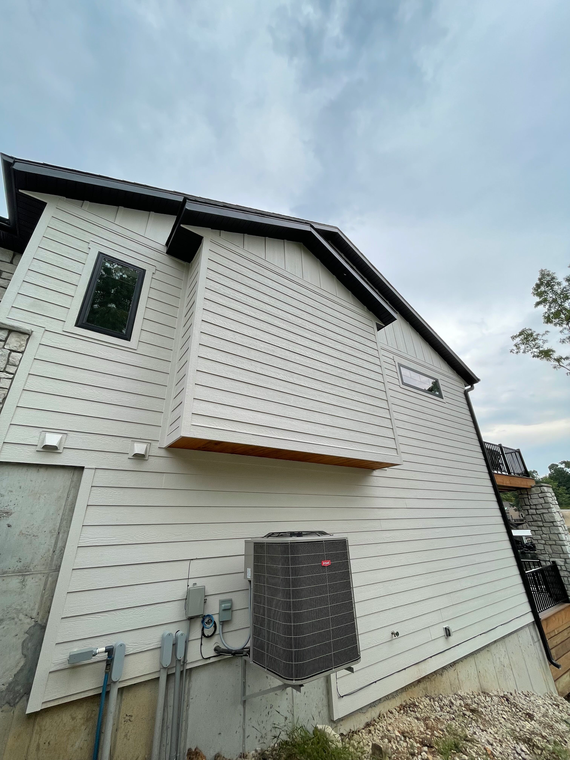 A white house with a black roof and a black air conditioner on the side of it.