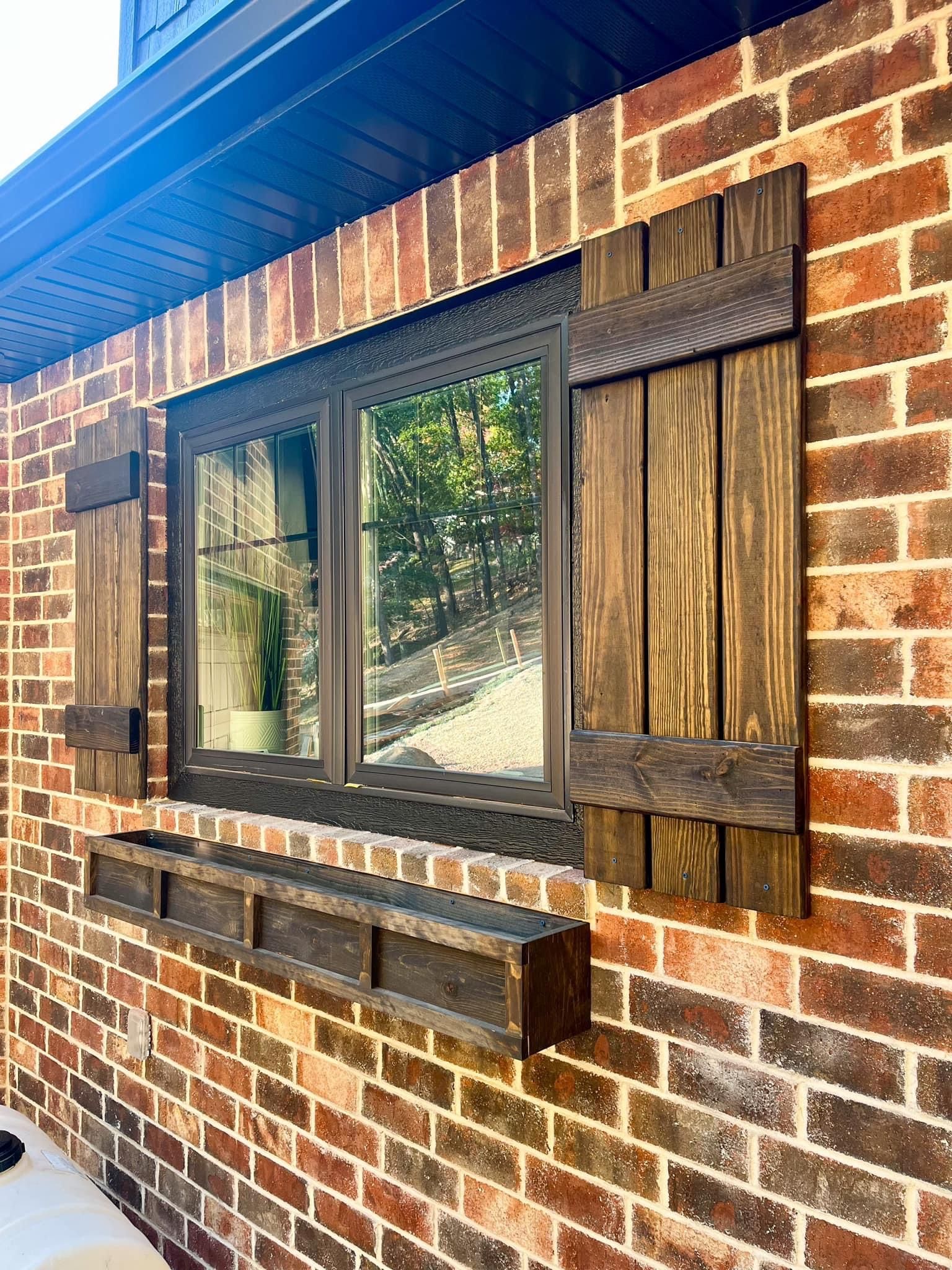 A brick wall with a window and wooden shutters on it.