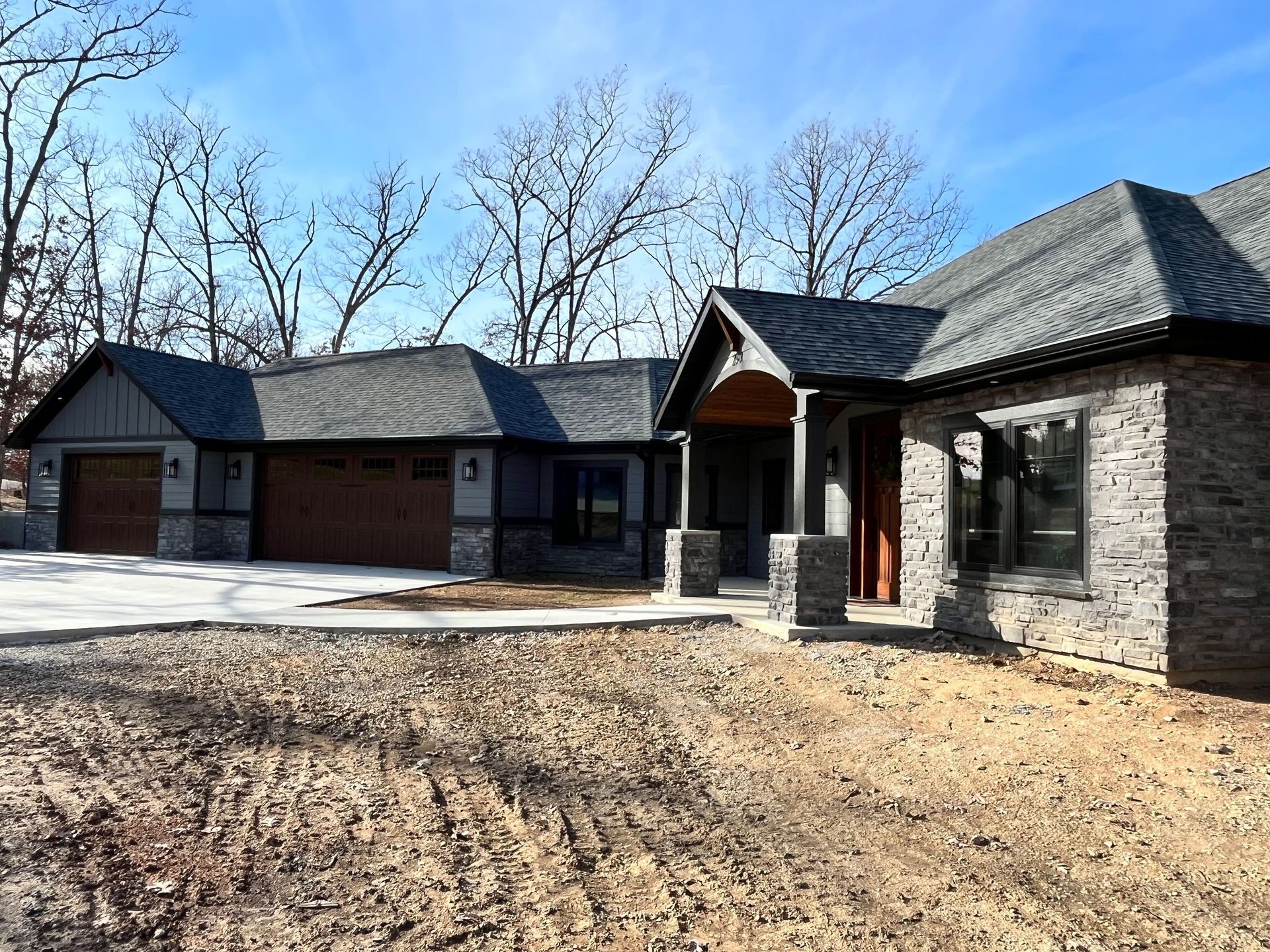 A large house with a gray roof is sitting on top of a dirt field.