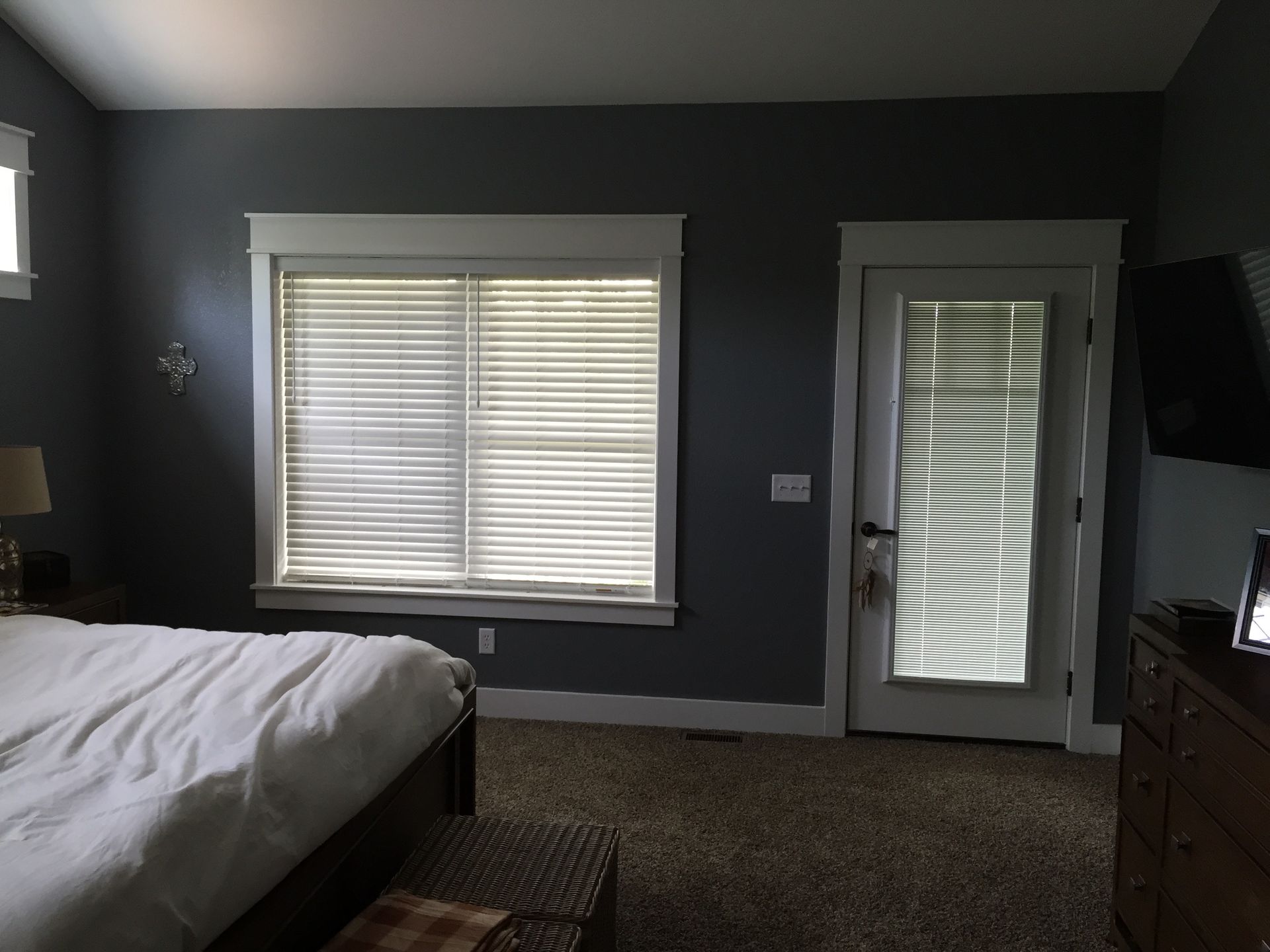 A bedroom with a bed , dresser , window and door.