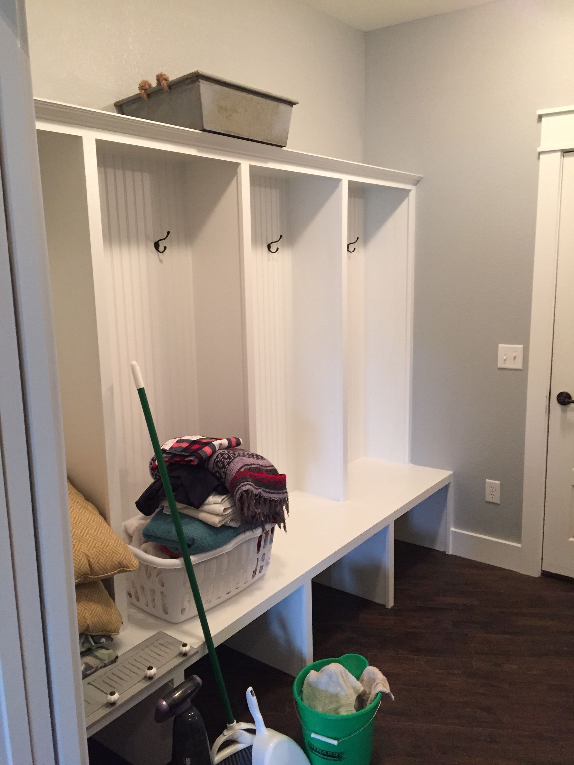 A mud room with a bench , a mop , and a bucket of cleaning supplies.