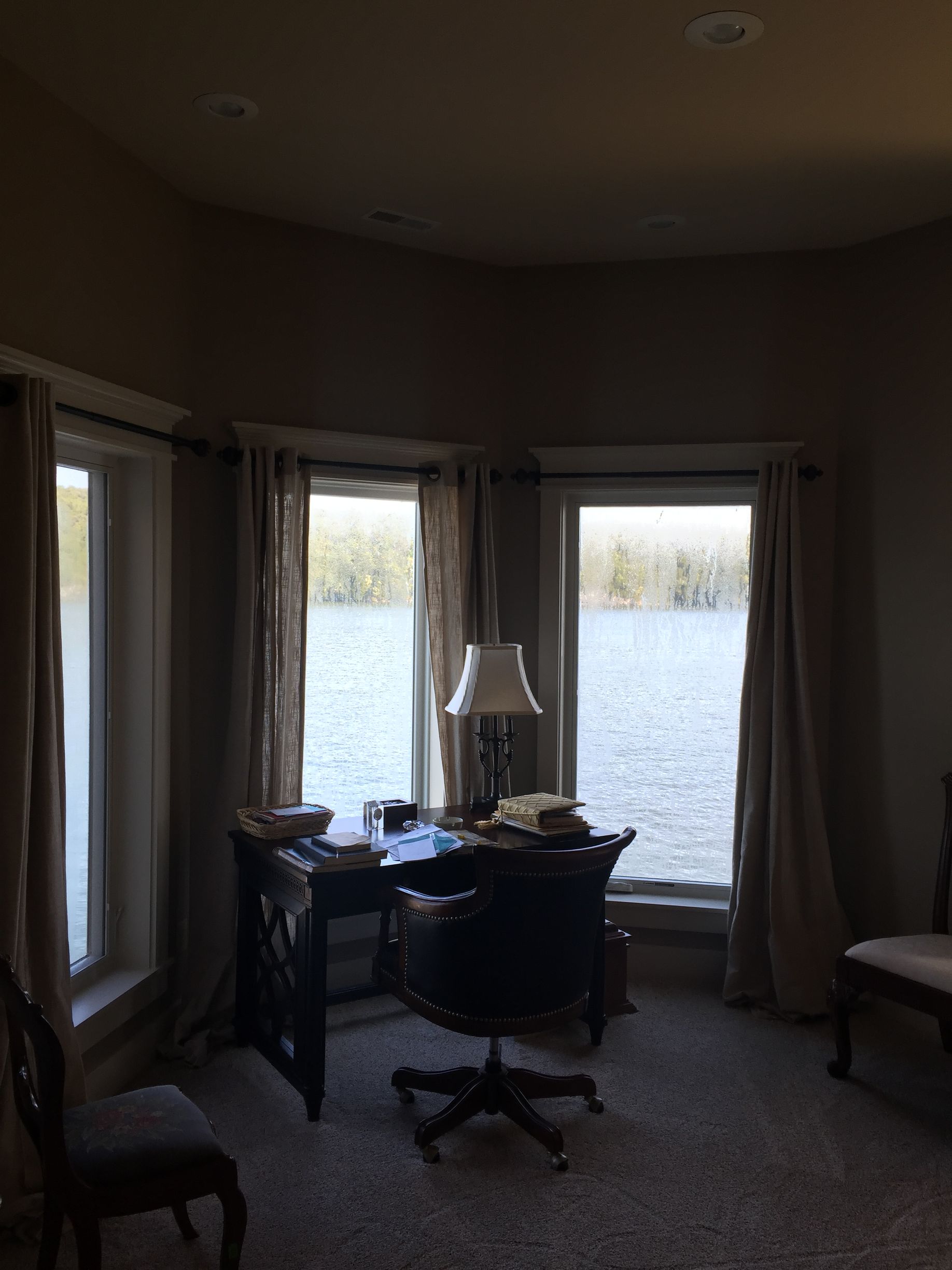 A dark room with a desk and chair with a view of a lake