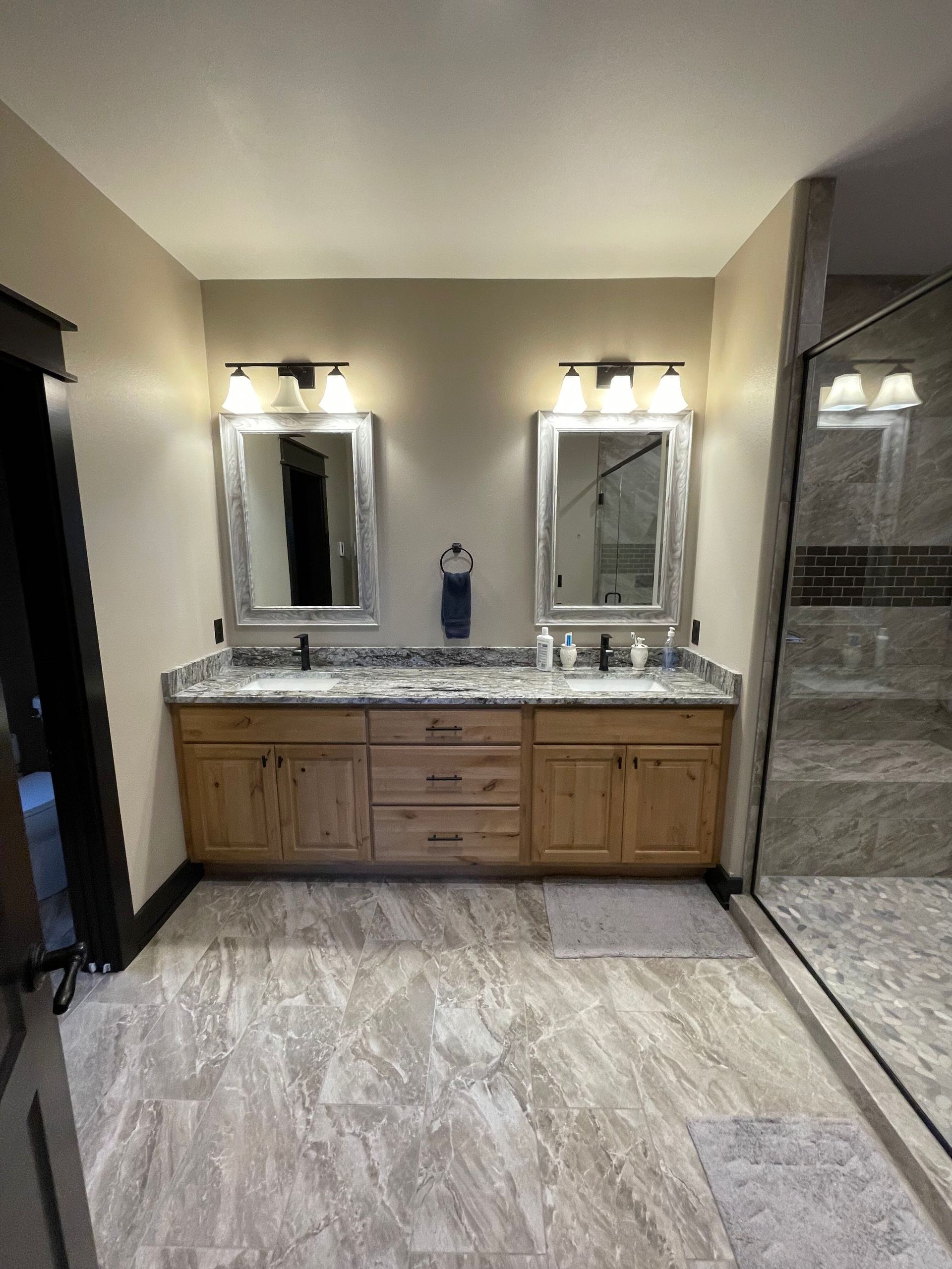 A bathroom with two sinks , two mirrors and a walk in shower.