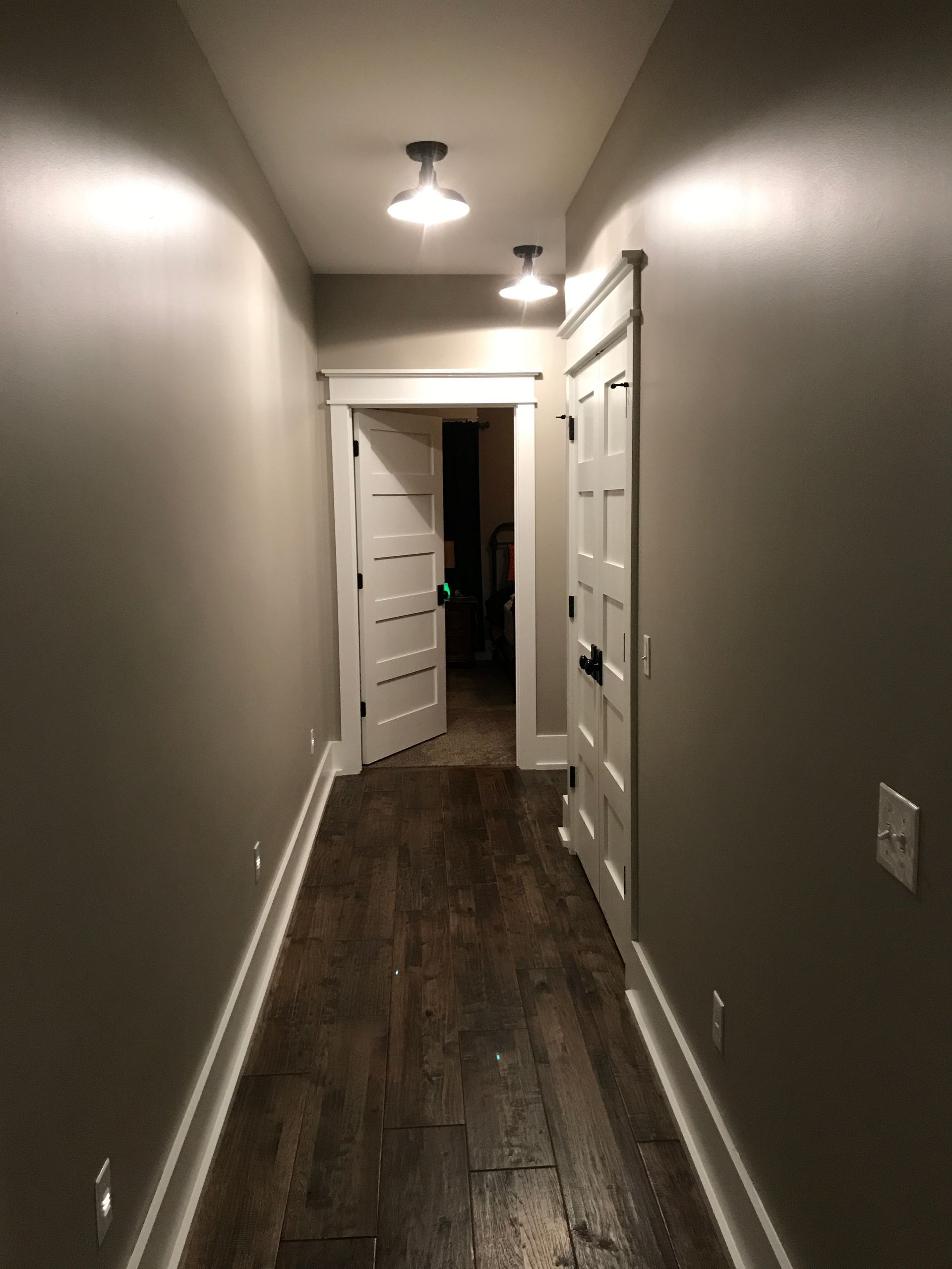 A long hallway with hardwood floors and gray walls leading to a door.