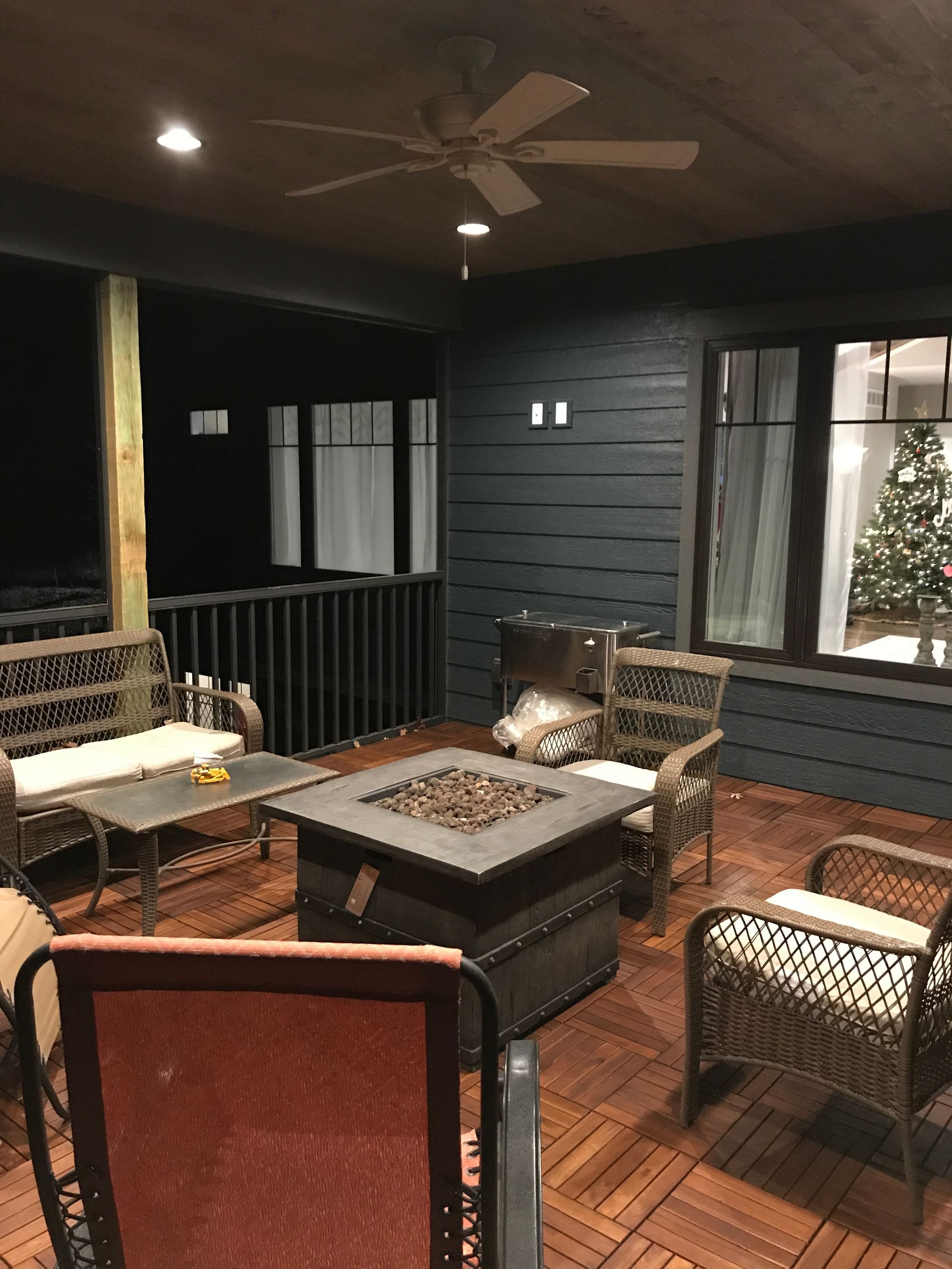 A patio with a fire pit , chairs , a table and a ceiling fan.