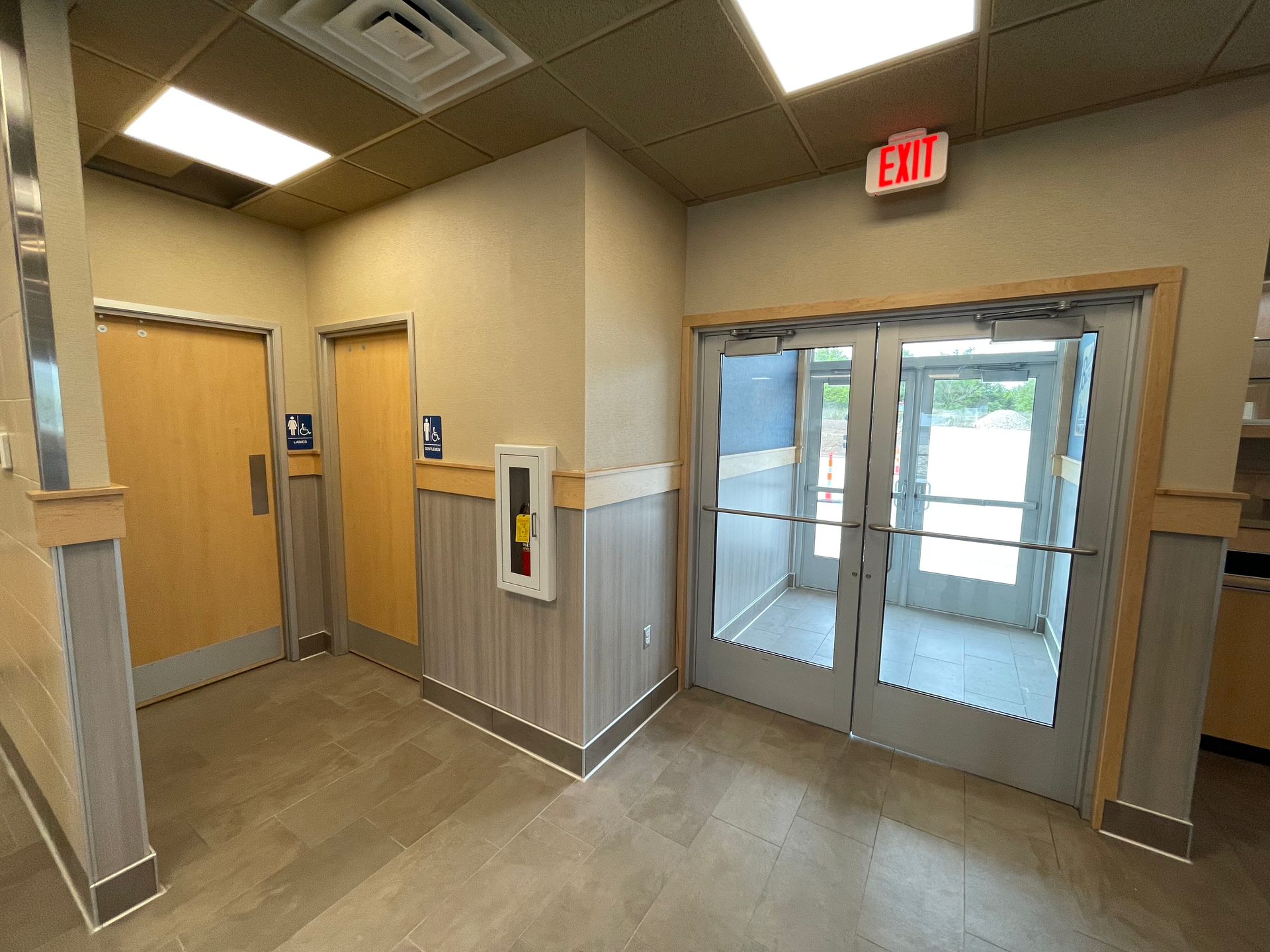 A hallway with a red exit sign above the doors.