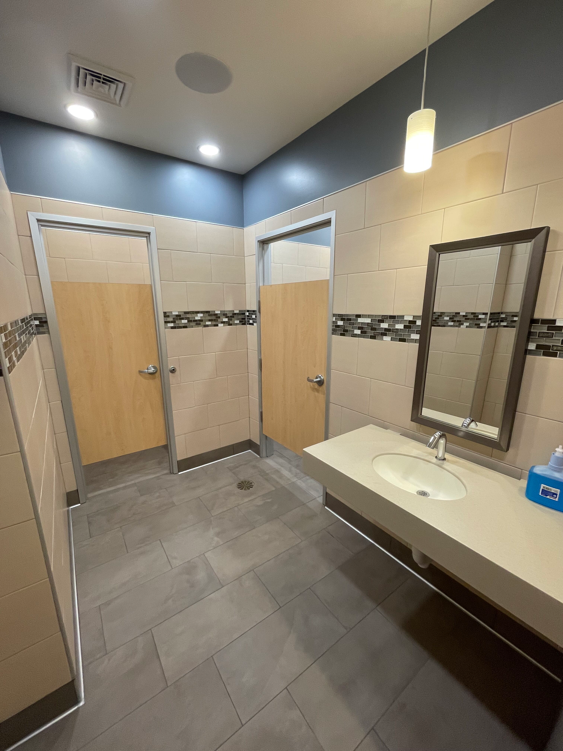 A bathroom with two stalls , a sink and a mirror.