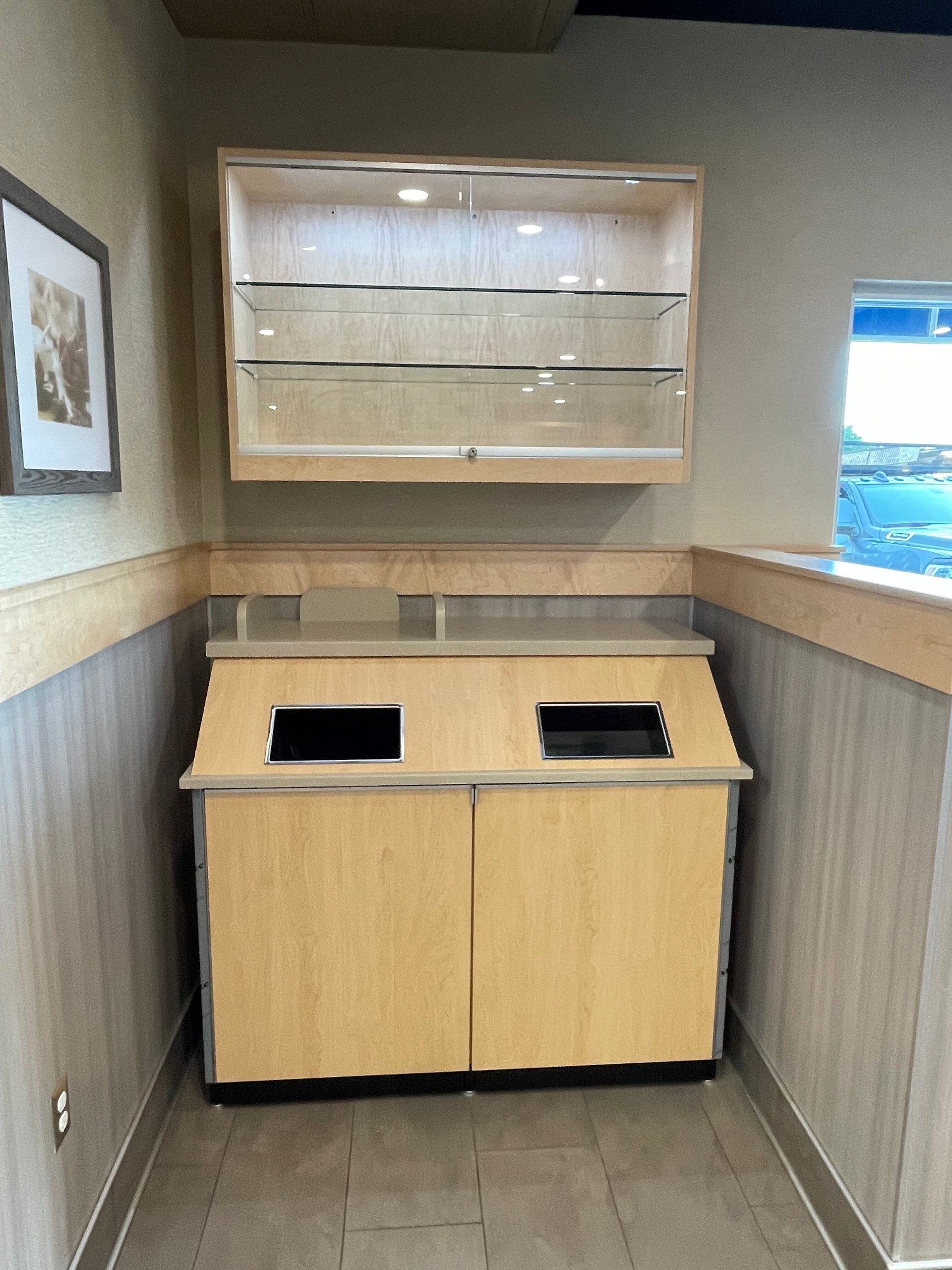 A corner of a room with a trash can and shelves