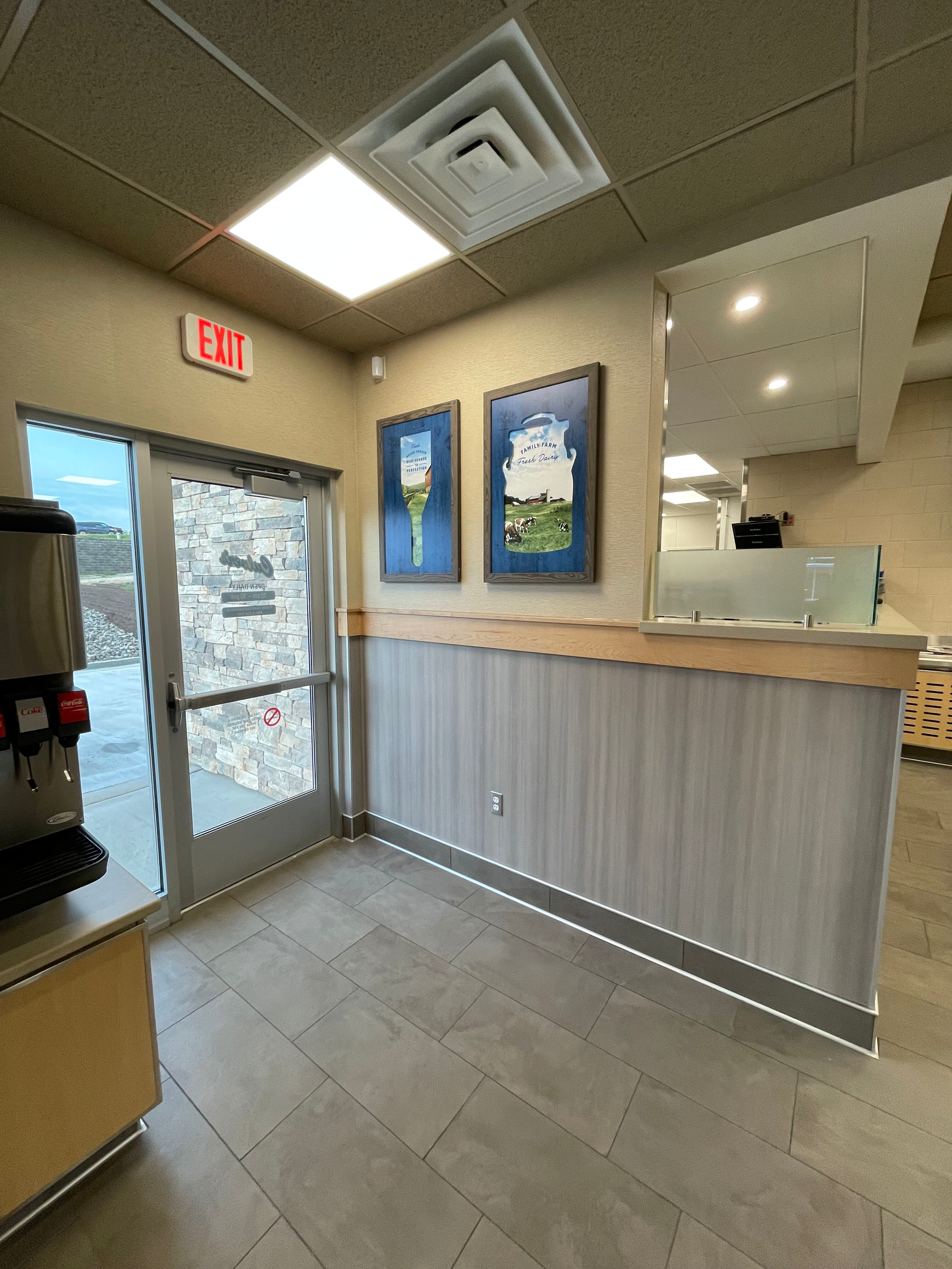 A room in a restaurant with a red exit sign on the wall.