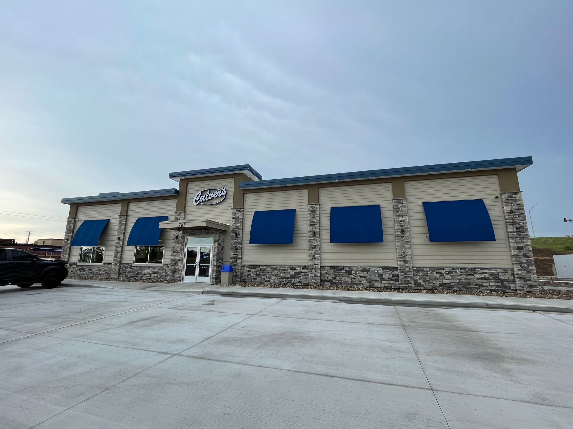 A building with blue awnings on the windows and a truck parked in front of it.