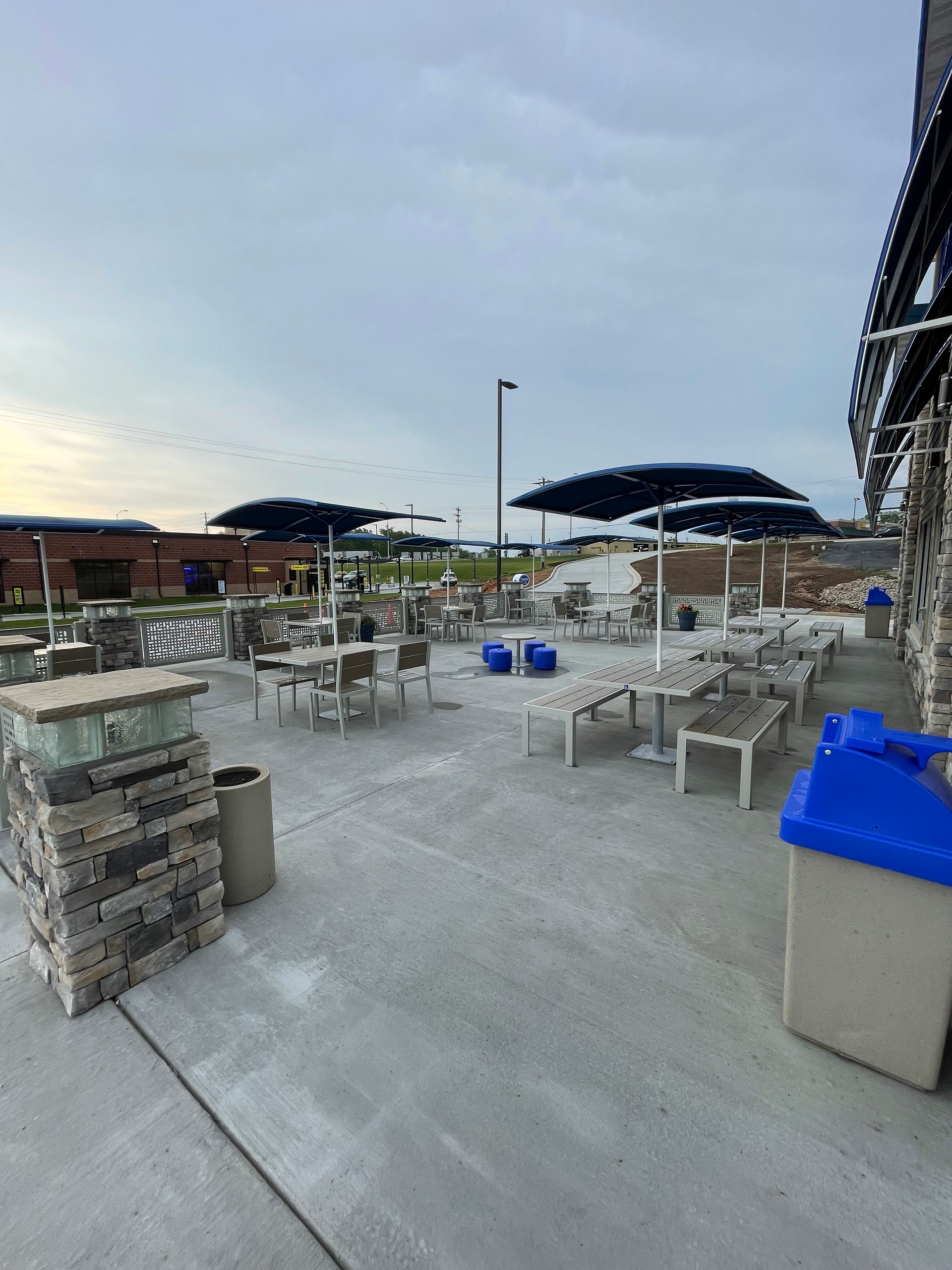 A patio with tables and umbrellas and a blue trash can