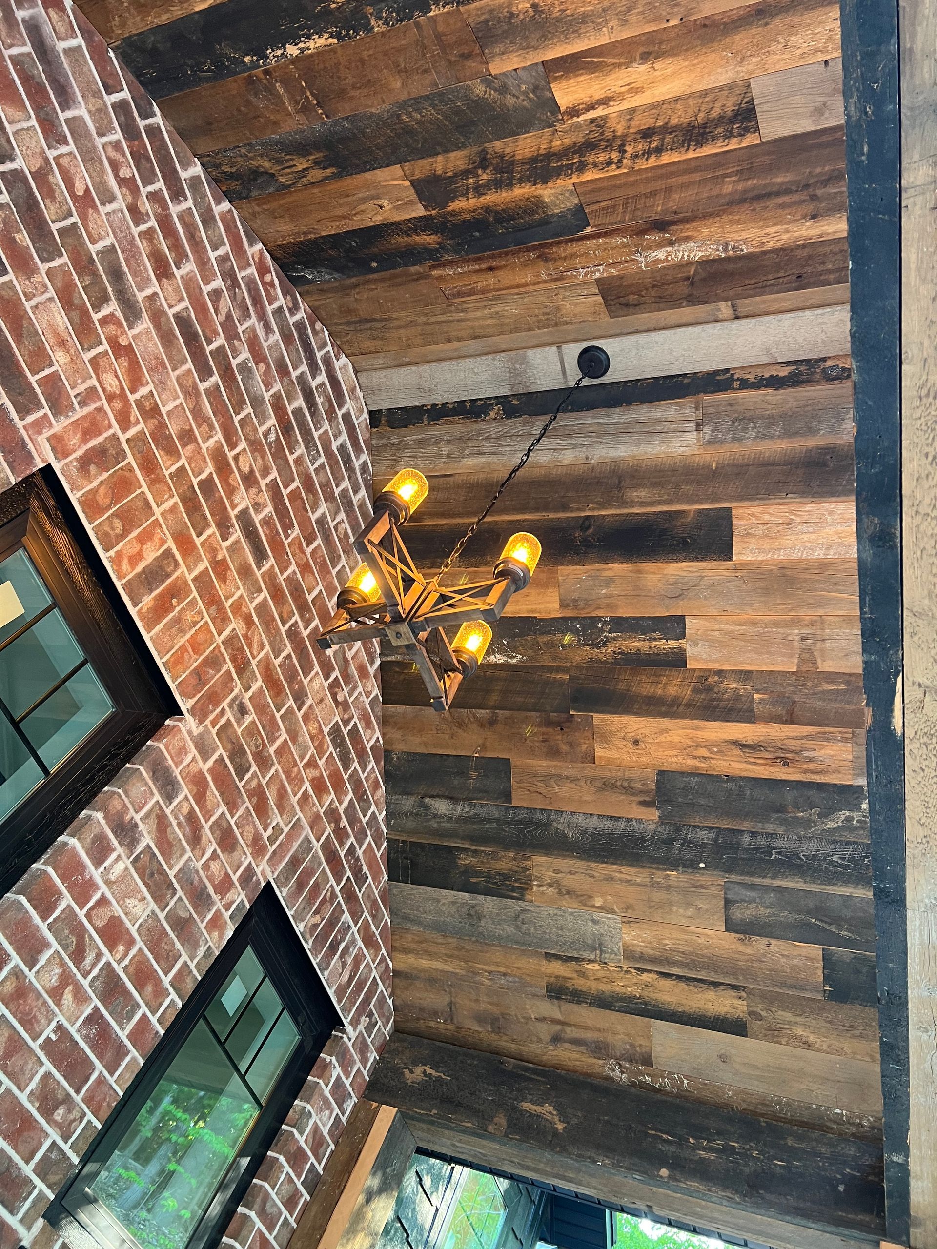 A wooden ceiling with a chandelier in a room with a brick wall.