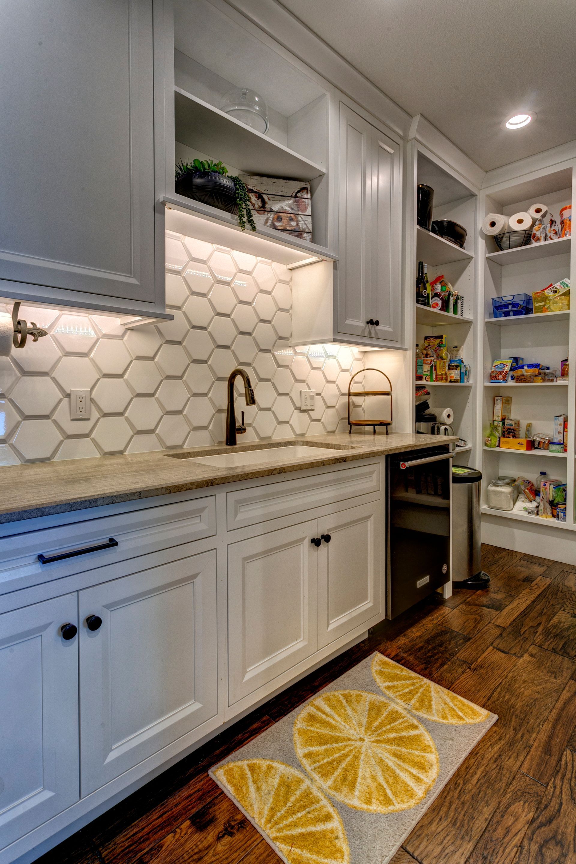 A kitchen with white cabinets , hardwood floors , a sink , and a rug with lemon slices on it.