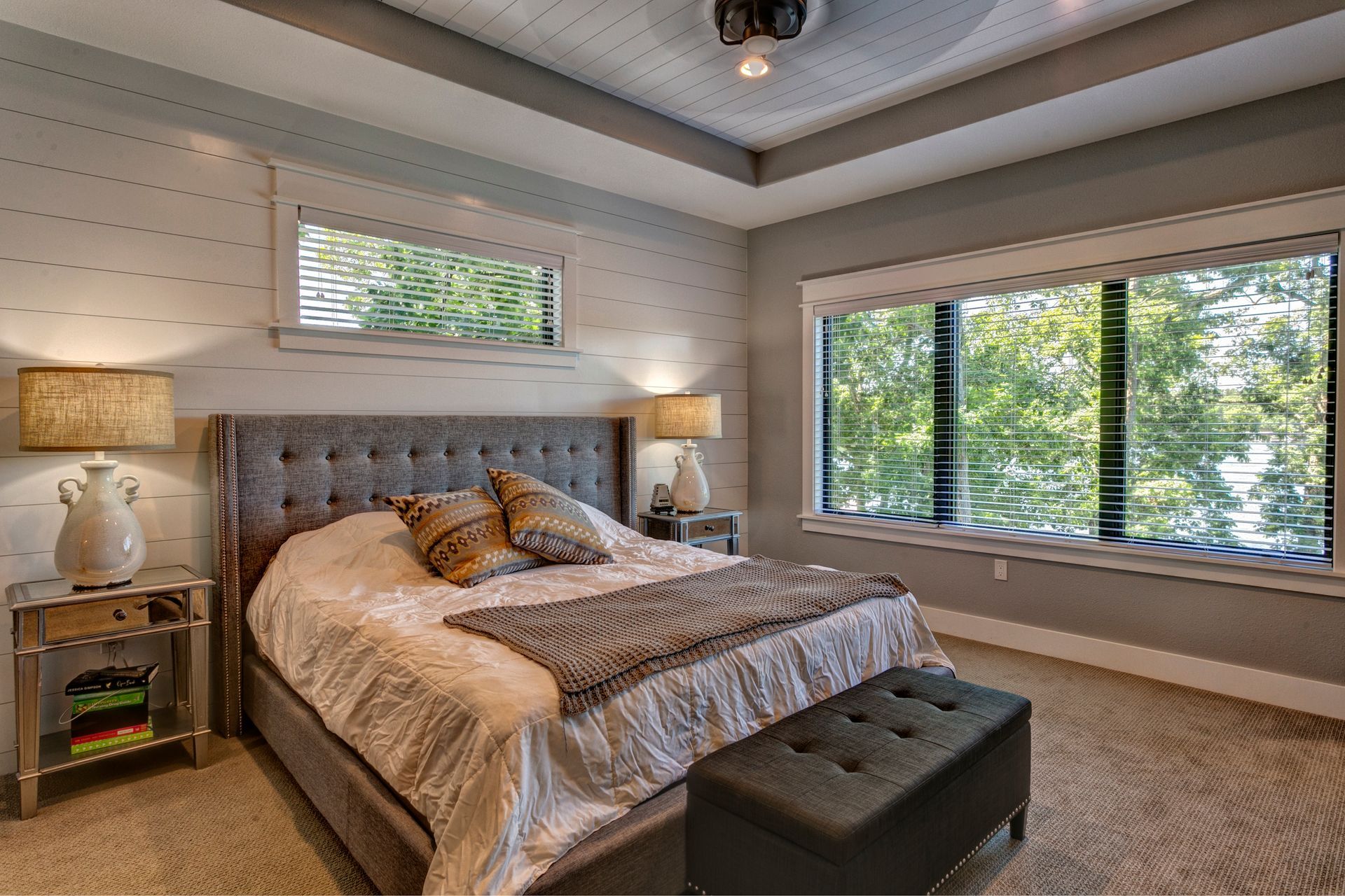 A bedroom with a large bed , two windows , lamps , and a bench.