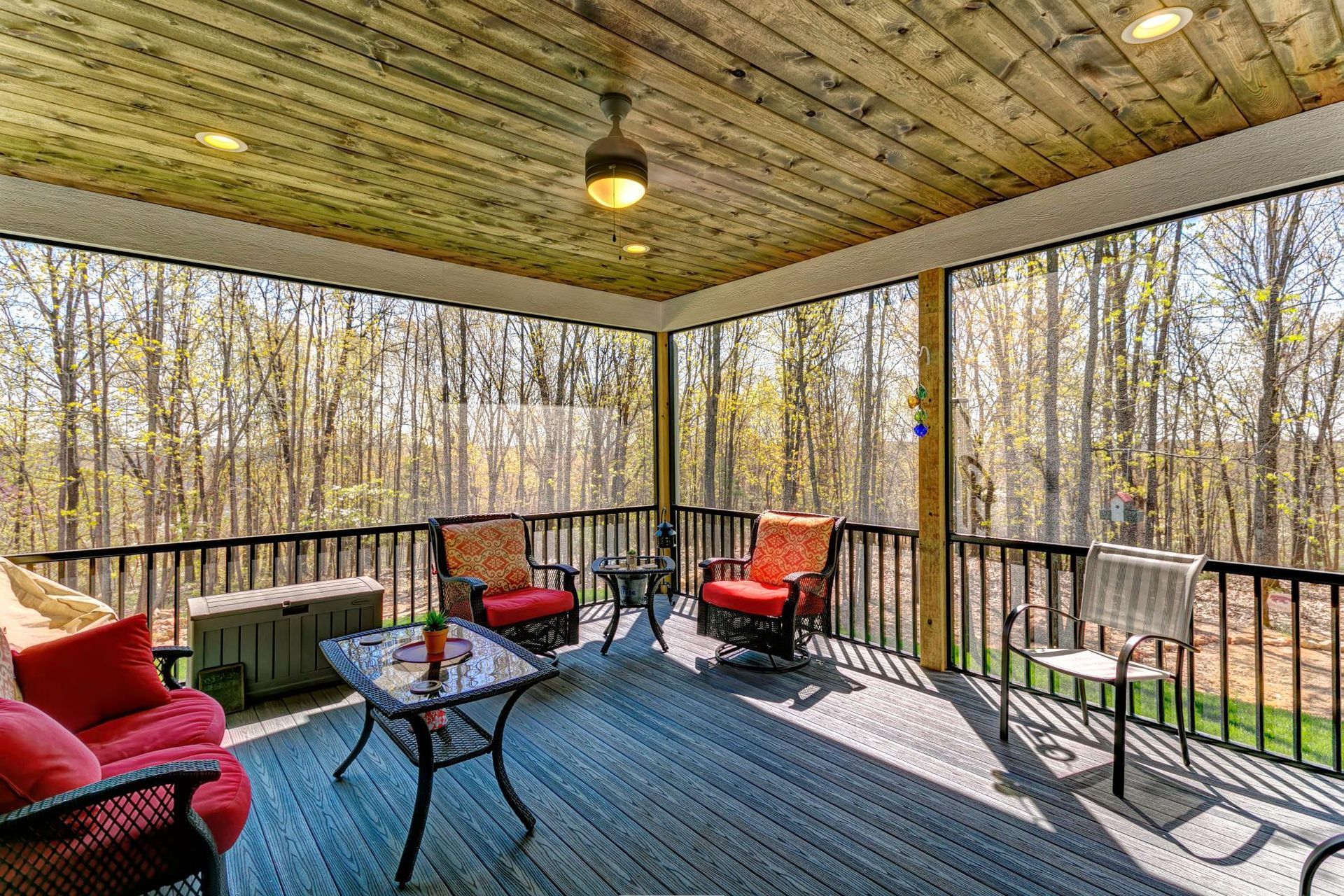 A screened in porch with chairs , a table and a ceiling fan.