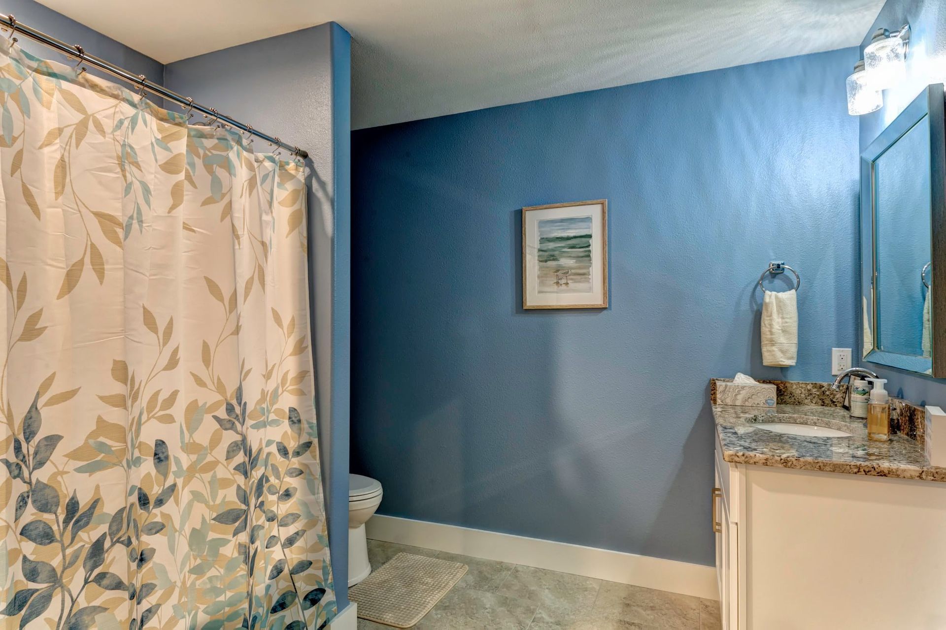 A bathroom with a shower curtain , toilet , sink and mirror.