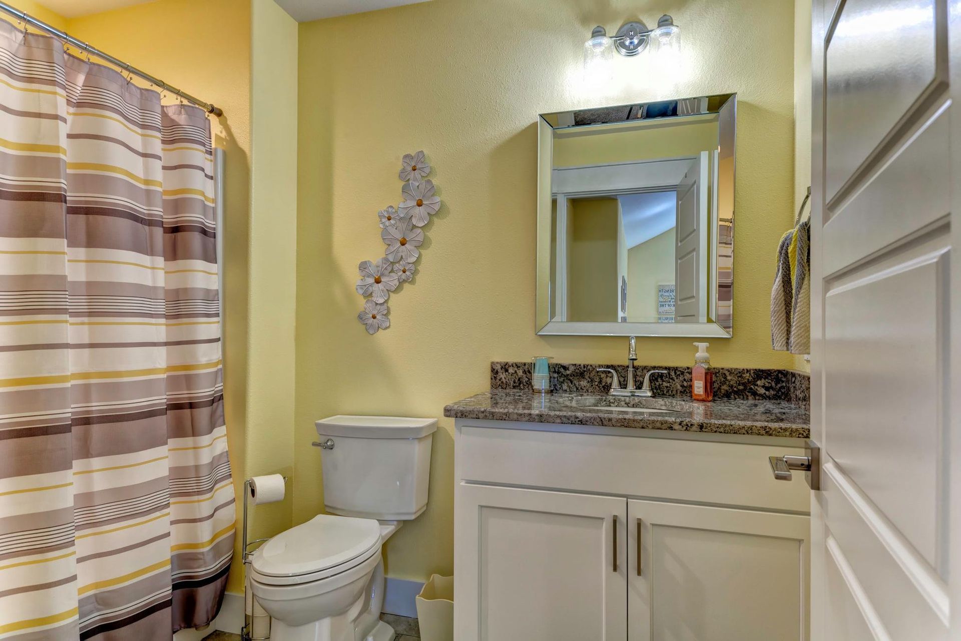 A bathroom with a toilet , sink , mirror and shower curtain.