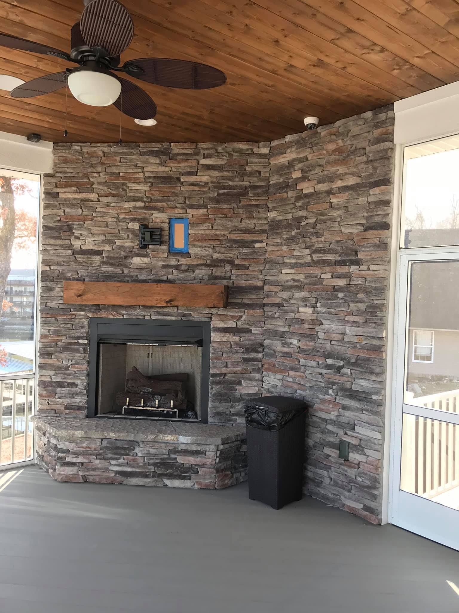 A screened in porch with a fireplace and a ceiling fan.