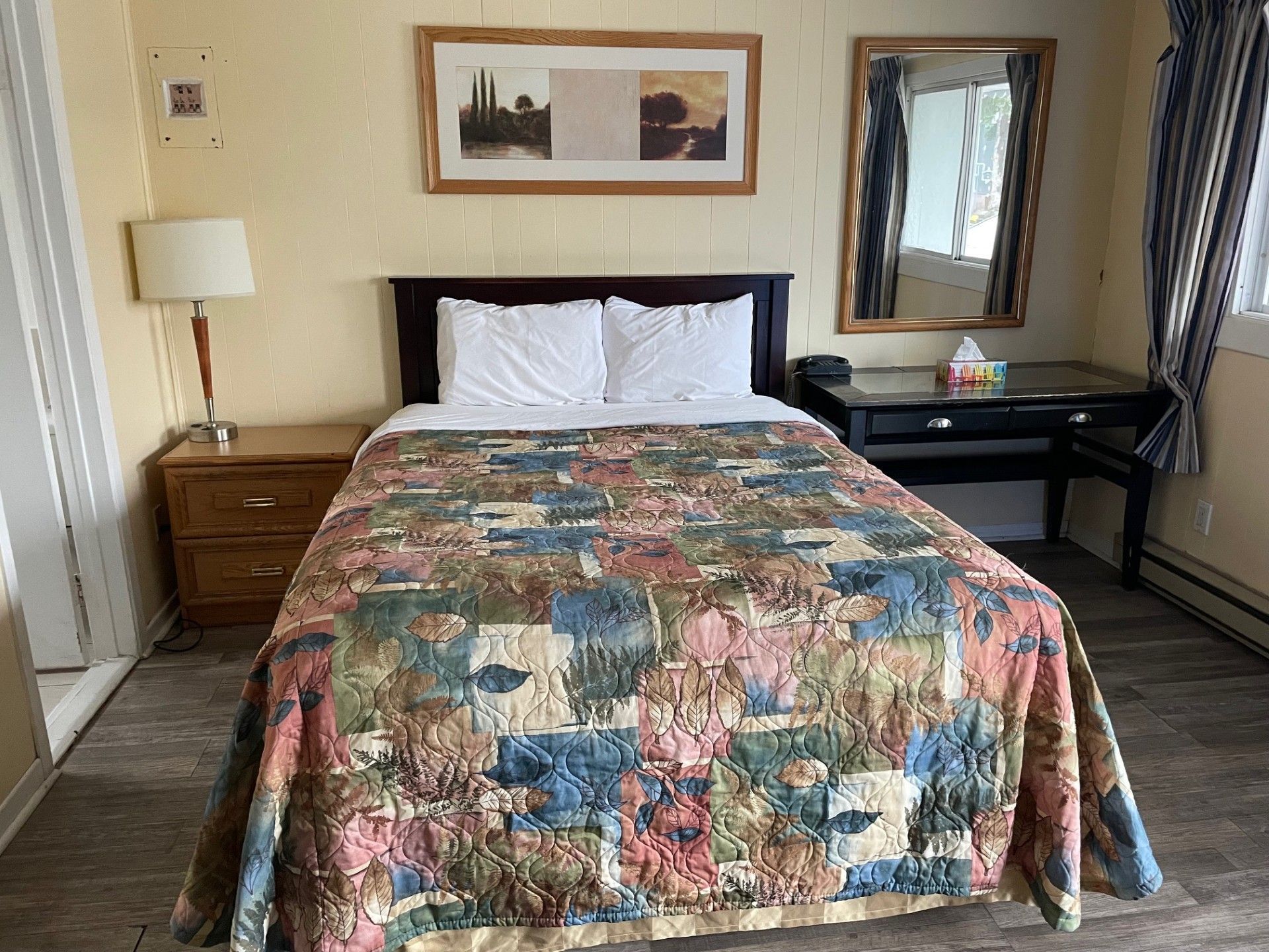 Une chambre d'hôtel avec un lit, une table de chevet, une lampe et un miroir.