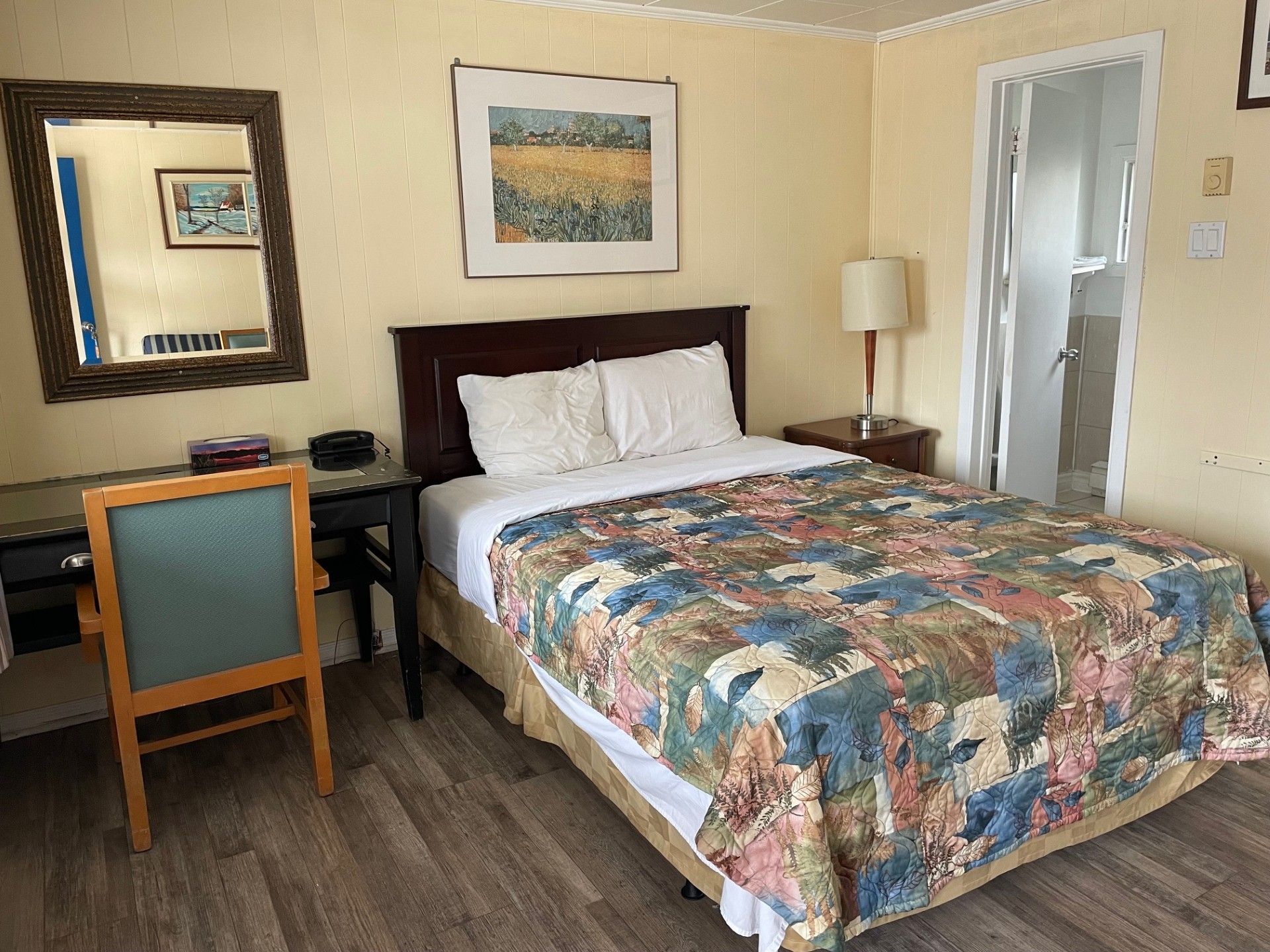 Une chambre d'hôtel avec un lit, un bureau, une chaise et un miroir.