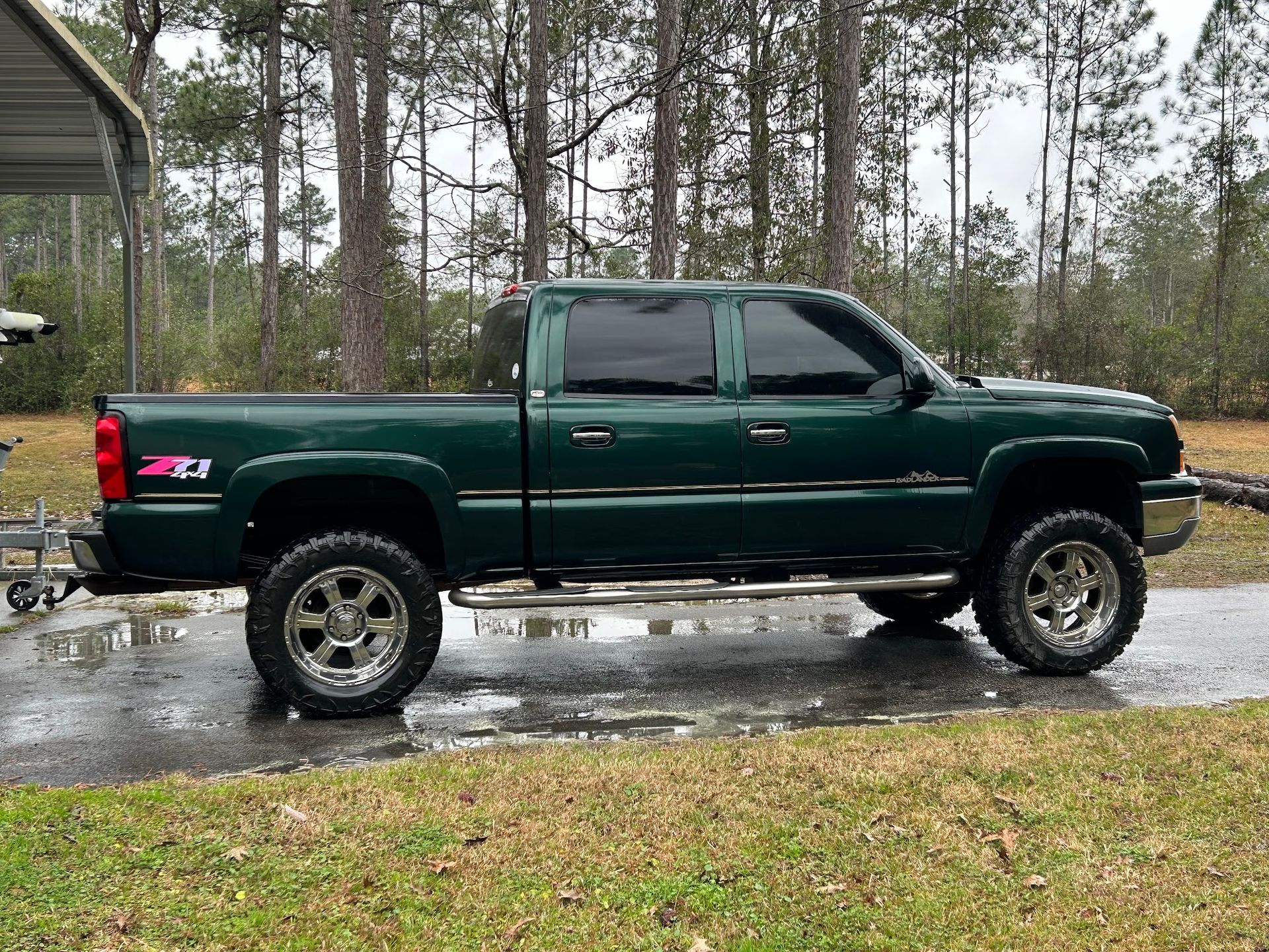 A green truck is parked on the side of the road next to a house.