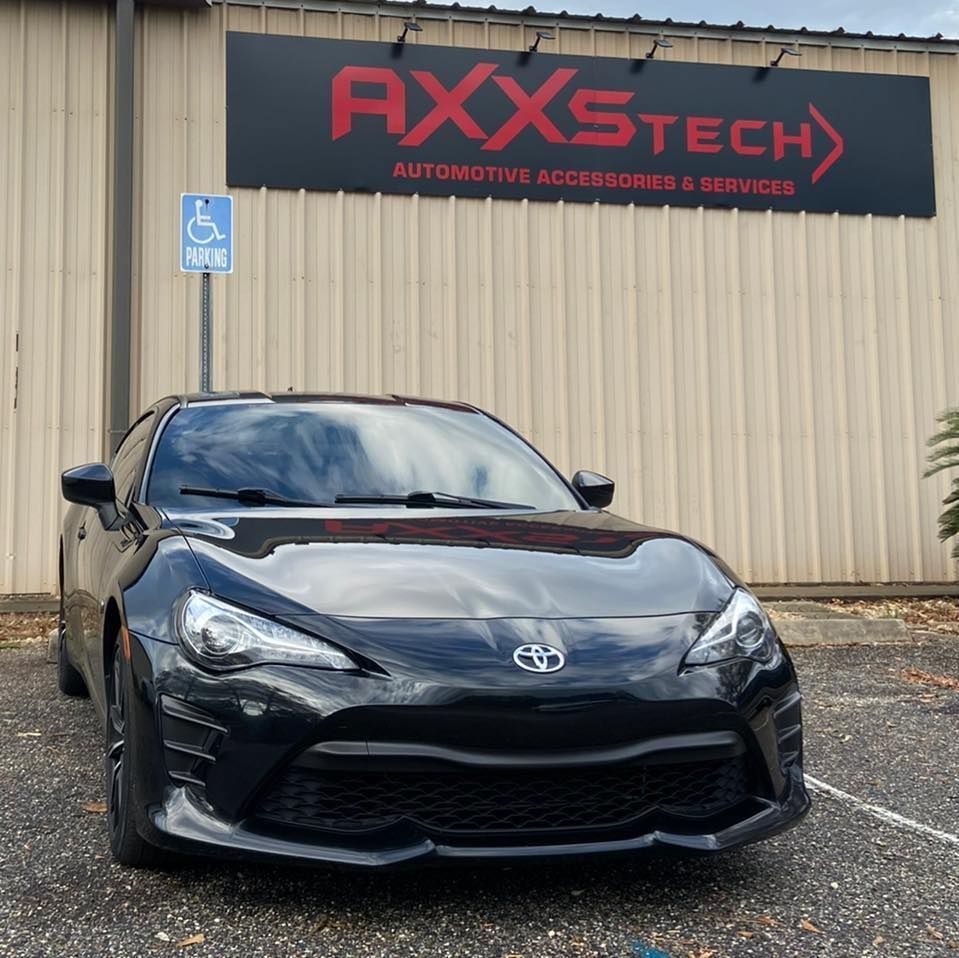 A black car is parked in front of a building that says axxtech