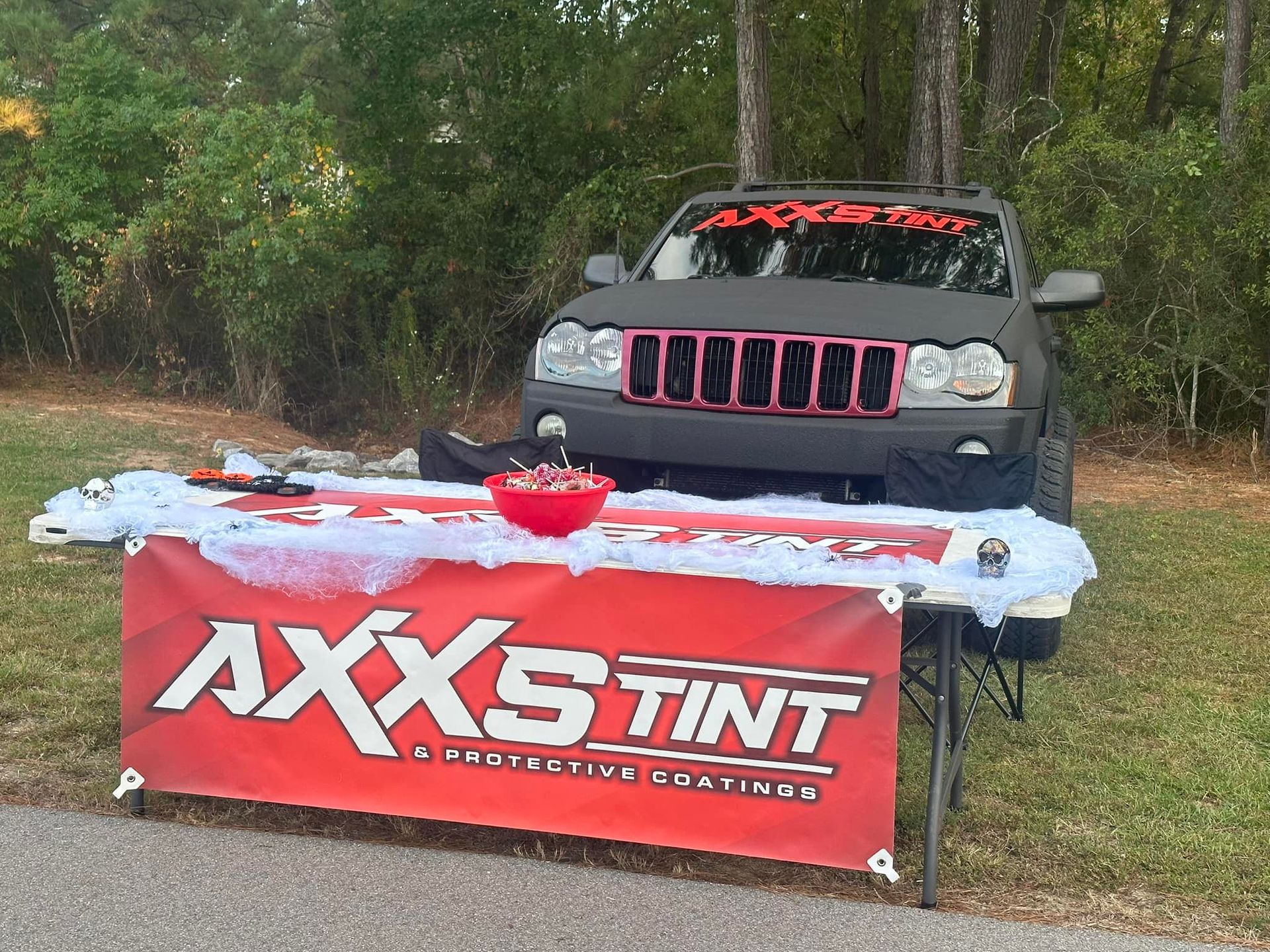 A jeep is parked in front of a table with a sign that says axxs tint