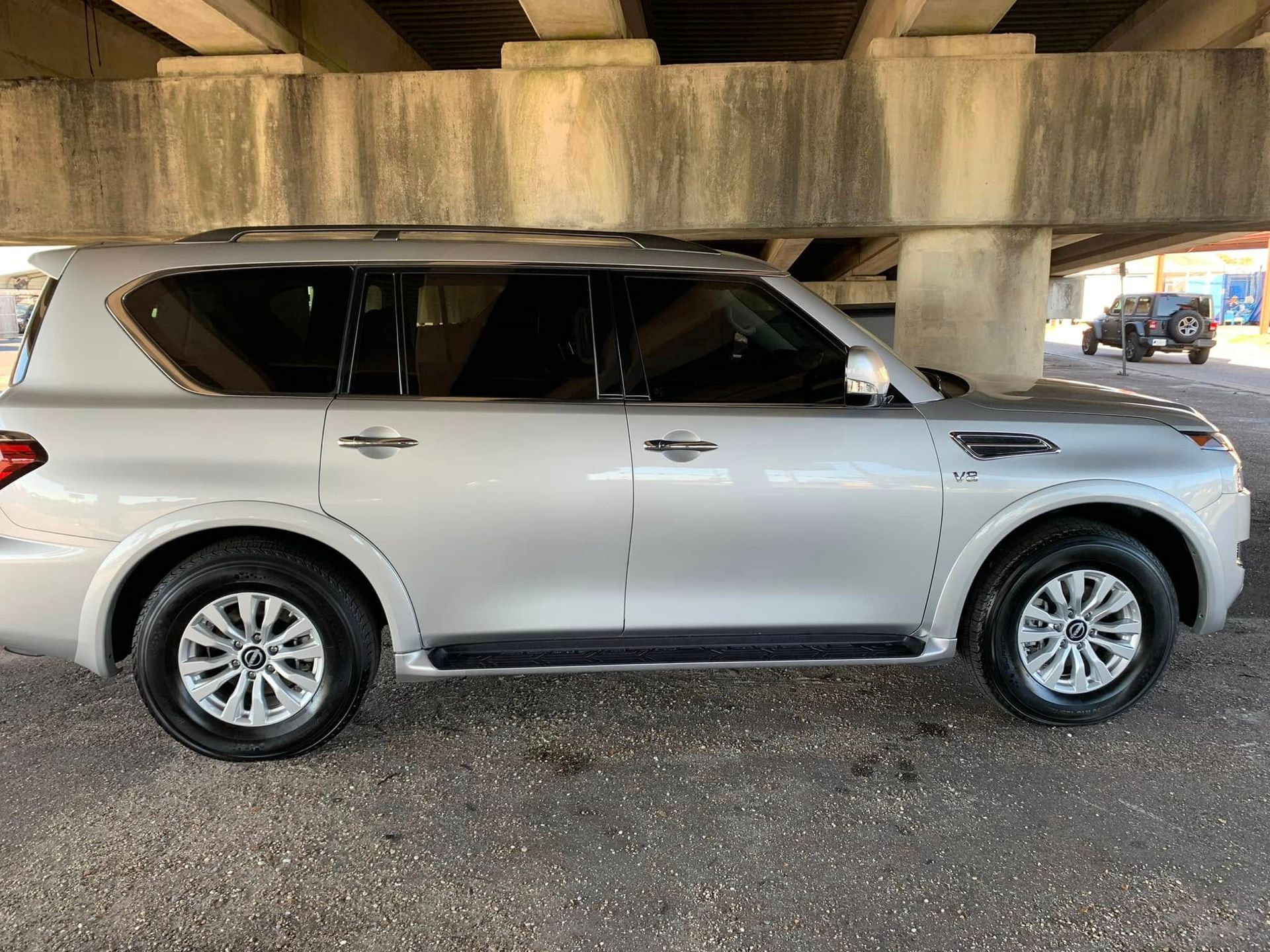 A silver nissan patrol is parked under a bridge.